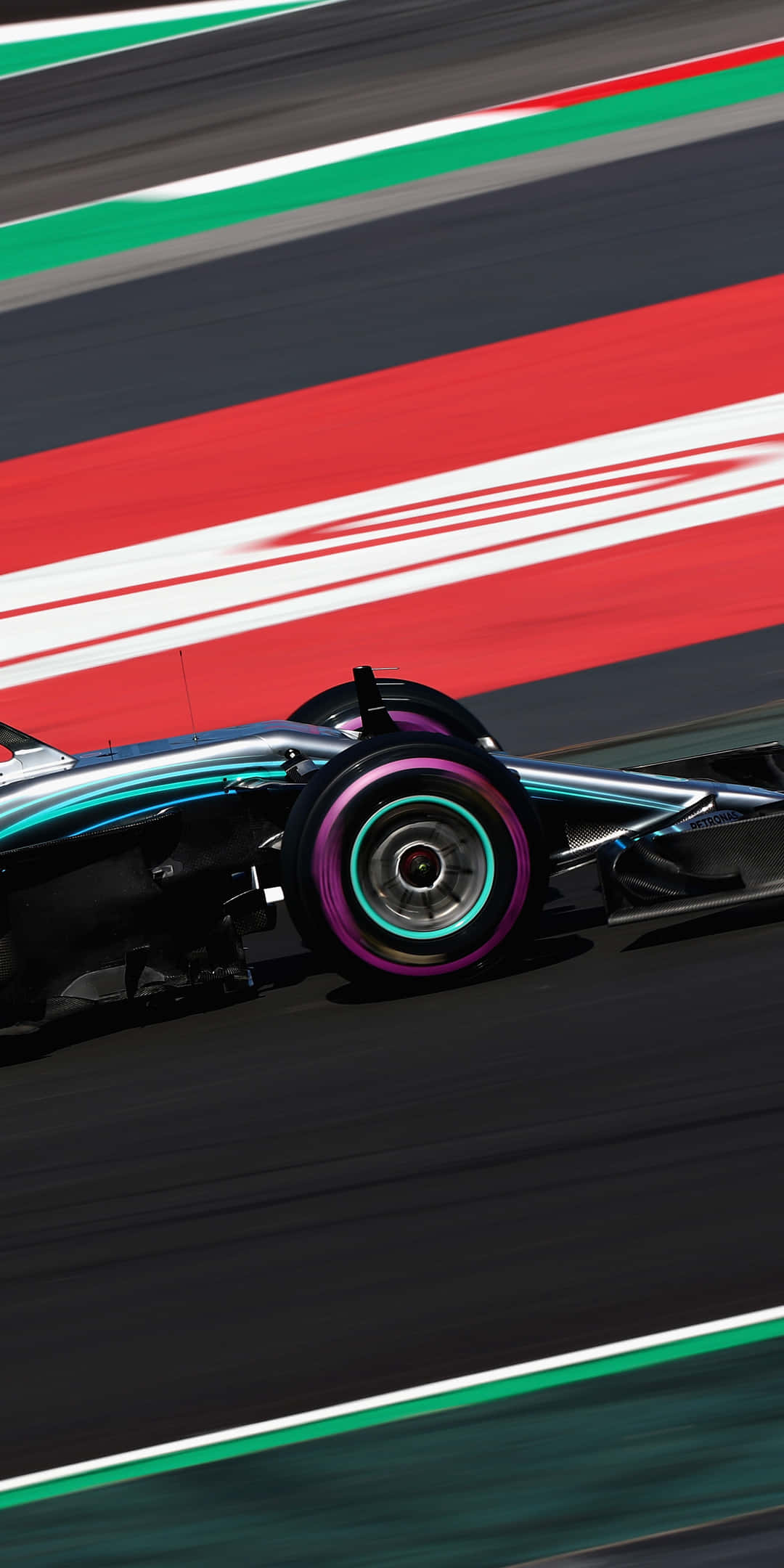 F1 桌布 壁紙 — 一輛流線型賽車在明亮的日光下，高速駛過一條有紅、白、綠條紋的賽道。