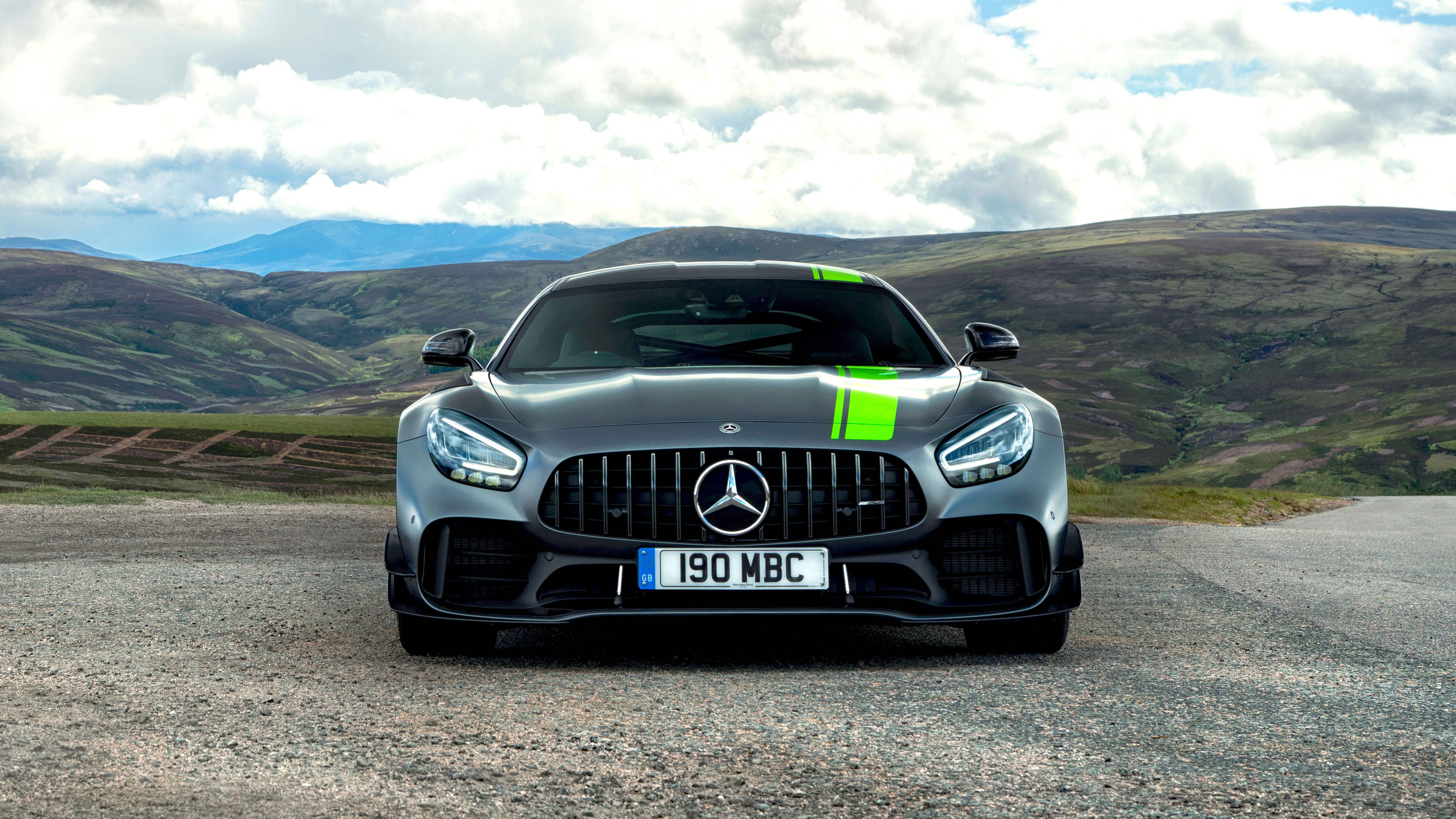 Gtr 桌布 壁紙 — 一輛流線型銀色 Mercedes-AMG GT 停放在碎石路上，背後是起伏的綠色山丘和多雲的天空。
