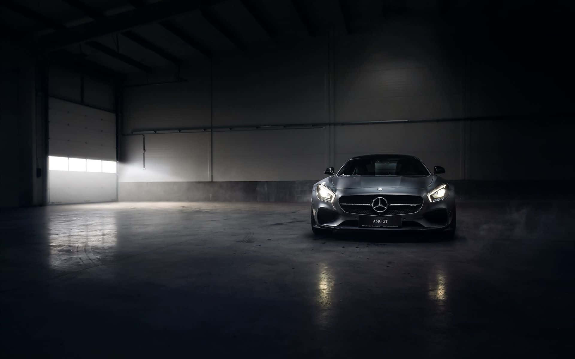 桌布 壁紙 — 一輛流線型銀色 Mercedes-AMG GT 跑車在寬敞昏暗的倉庫中，在混凝土地板和工業橫樑下，於戲劇性的聚光燈下閃耀。