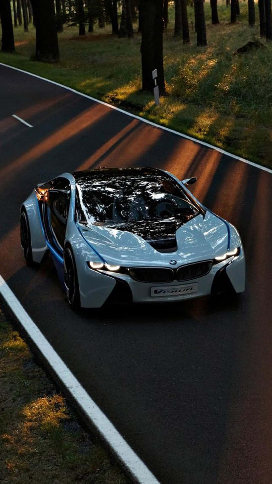 高清汽車 桌布 壁紙 — 一輛流線型銀色BMW i8 Vision跑車沿著沐浴在金色日落光中的森林道路行駛。