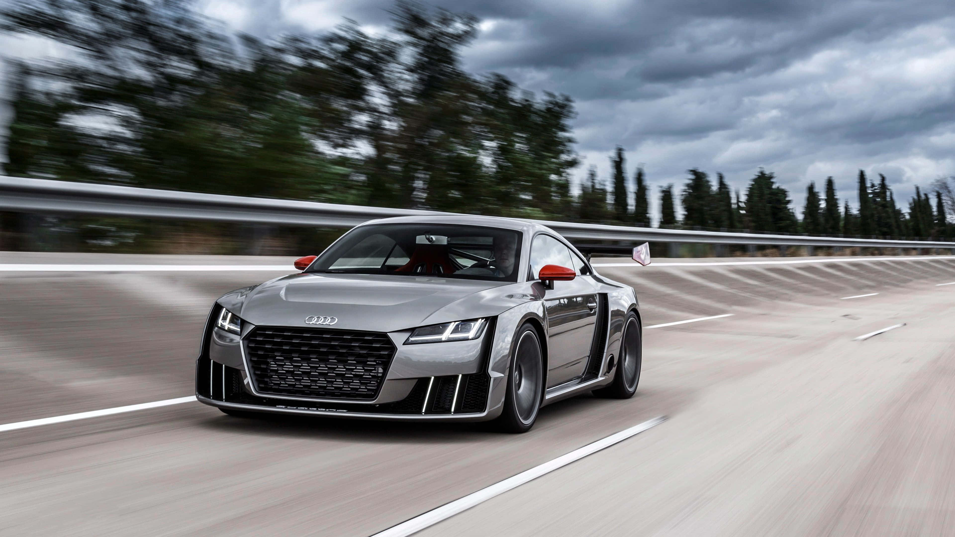 Audi Tt 桌布 壁紙 — 一輛流線型銀色奧迪R8在蜿蜒的高速公路上疾駛，背景是模糊的樹木和陰天。