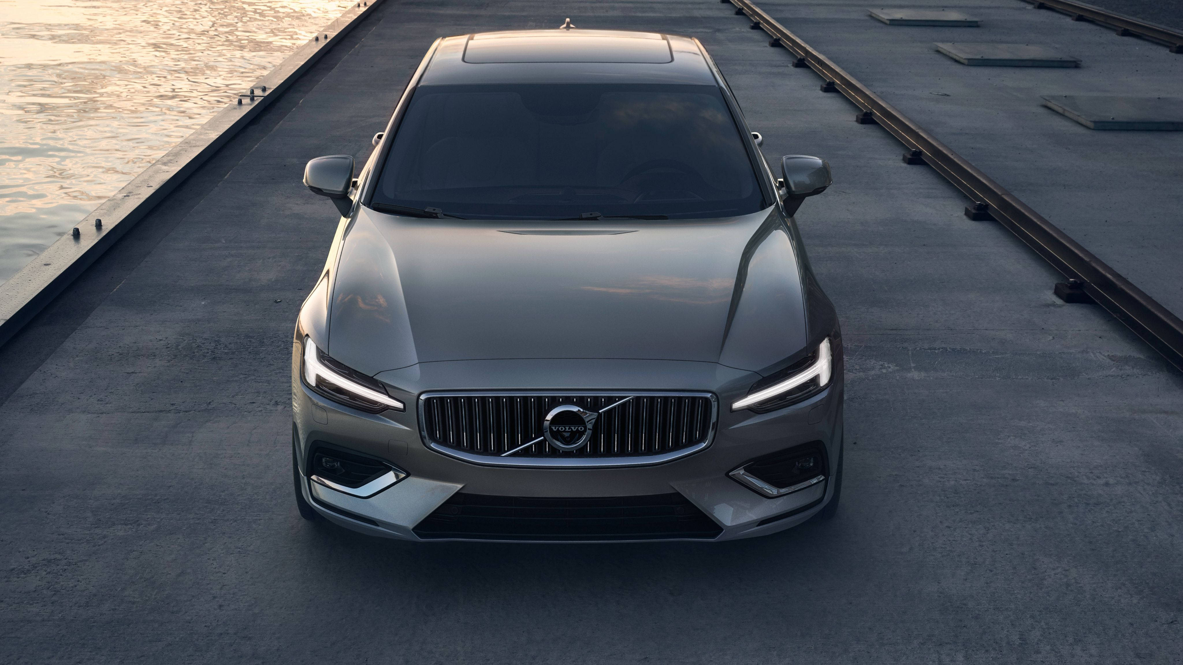 Volvo 桌布 壁紙 — 一輛流線型銀色富豪房車在柔和黃金時段的光線下，面向前方停在平靜水邊的混凝土碼頭上。
