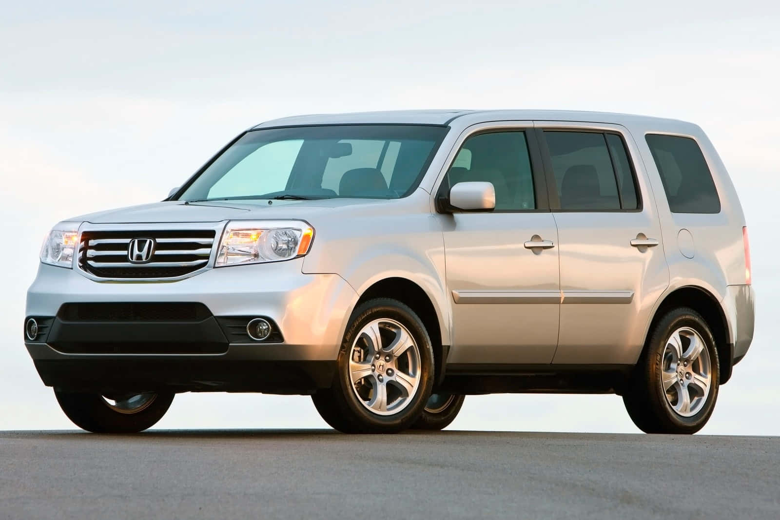 Honda Pilot 桌布 壁紙 — 一輛流線型銀色本田 Pilot SUV 停放在平坦表面上，柔和日光下，背景是晴朗天空。