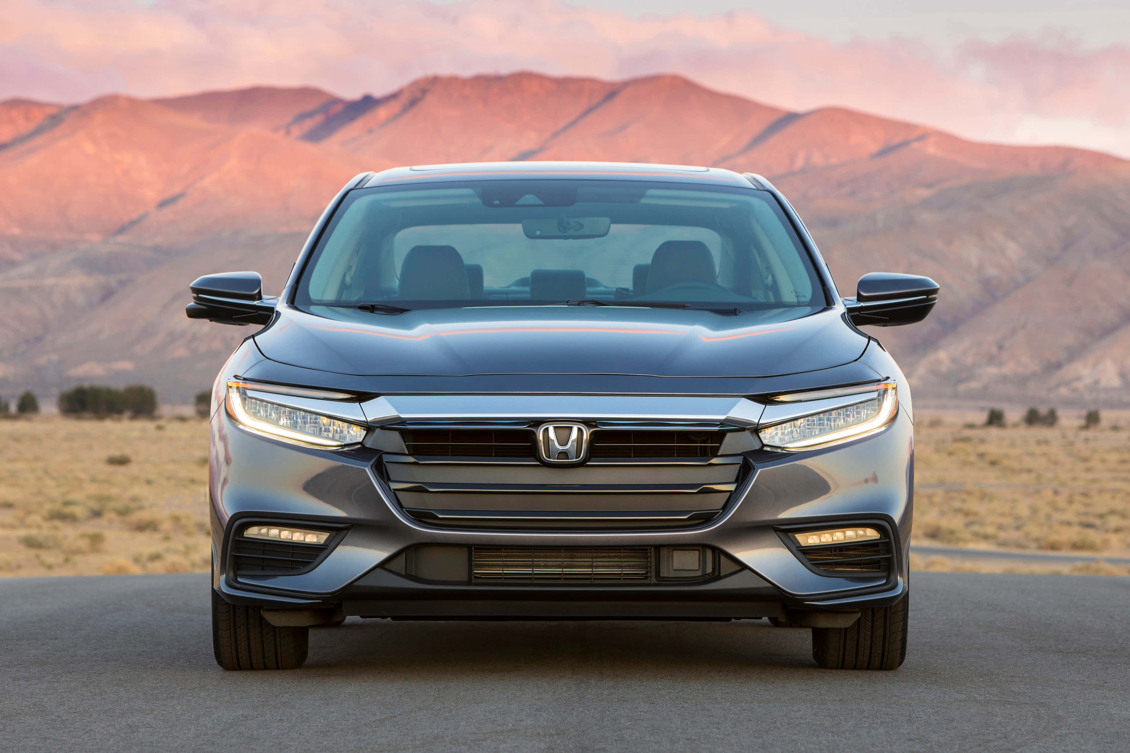 Honda Insight 桌布 壁紙 — 一輛流線型銀色本田轎車在沙漠公路上向前行駛，背後是粉紅色和橙色夕陽照耀的山巒。