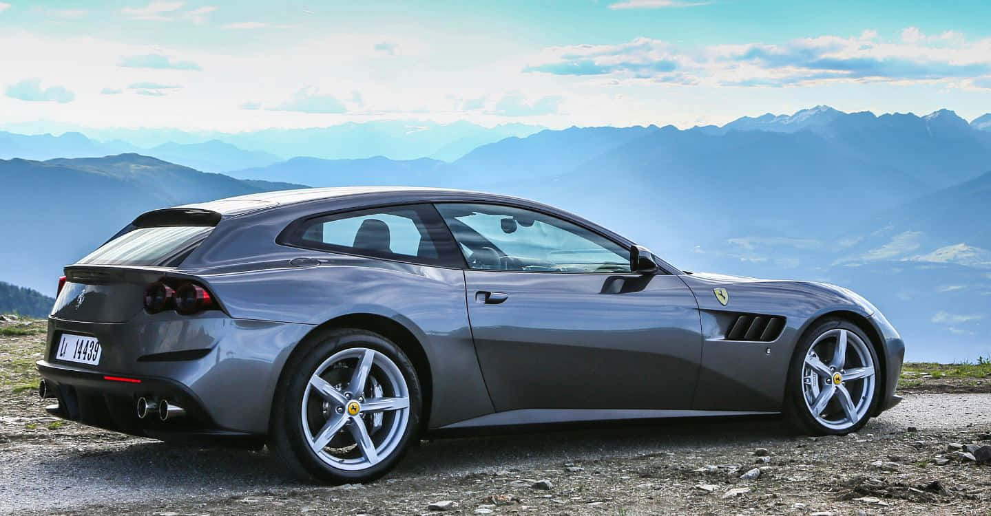 Ferrari Gtc4lusso 桌布 壁紙 — 一輛流線型銀色法拉利停泊在山頂觀景點，背景是分層的藍色山峰，天空局部多雲。