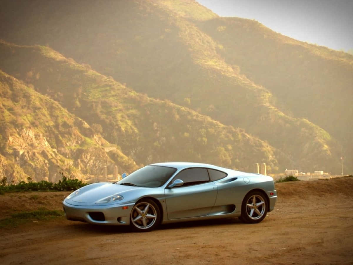 Ferrari 360 Modena 桌布 壁紙 — 一輛流線型銀色跑車停泊在塵土飛揚的路邊，背景是陽光普照的連綿山丘。