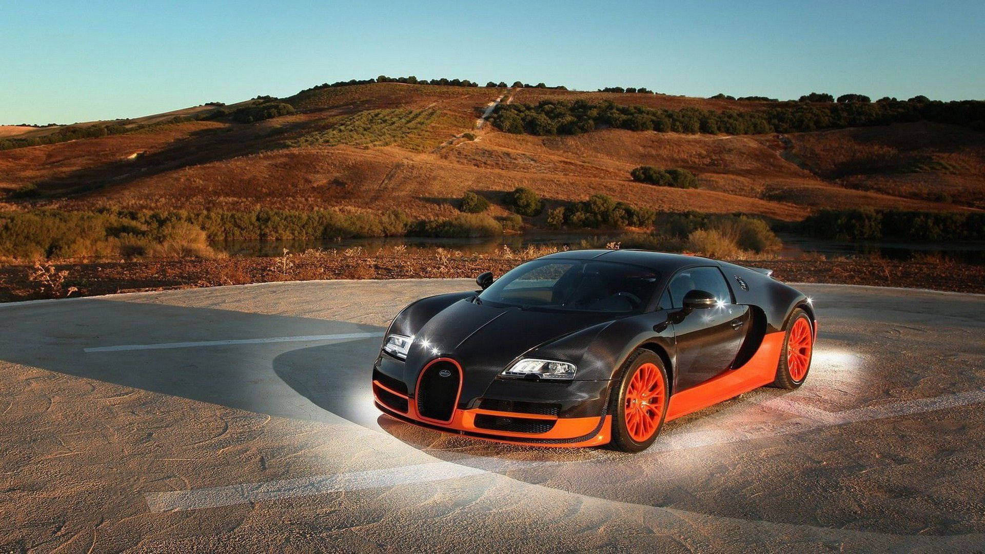 高清 桌布 壁紙 — 一輛流線型黑橙色Bugatti Veyron在彎曲道路上閃耀，沐浴在金色夕陽光下，背景是起伏的丘陵。