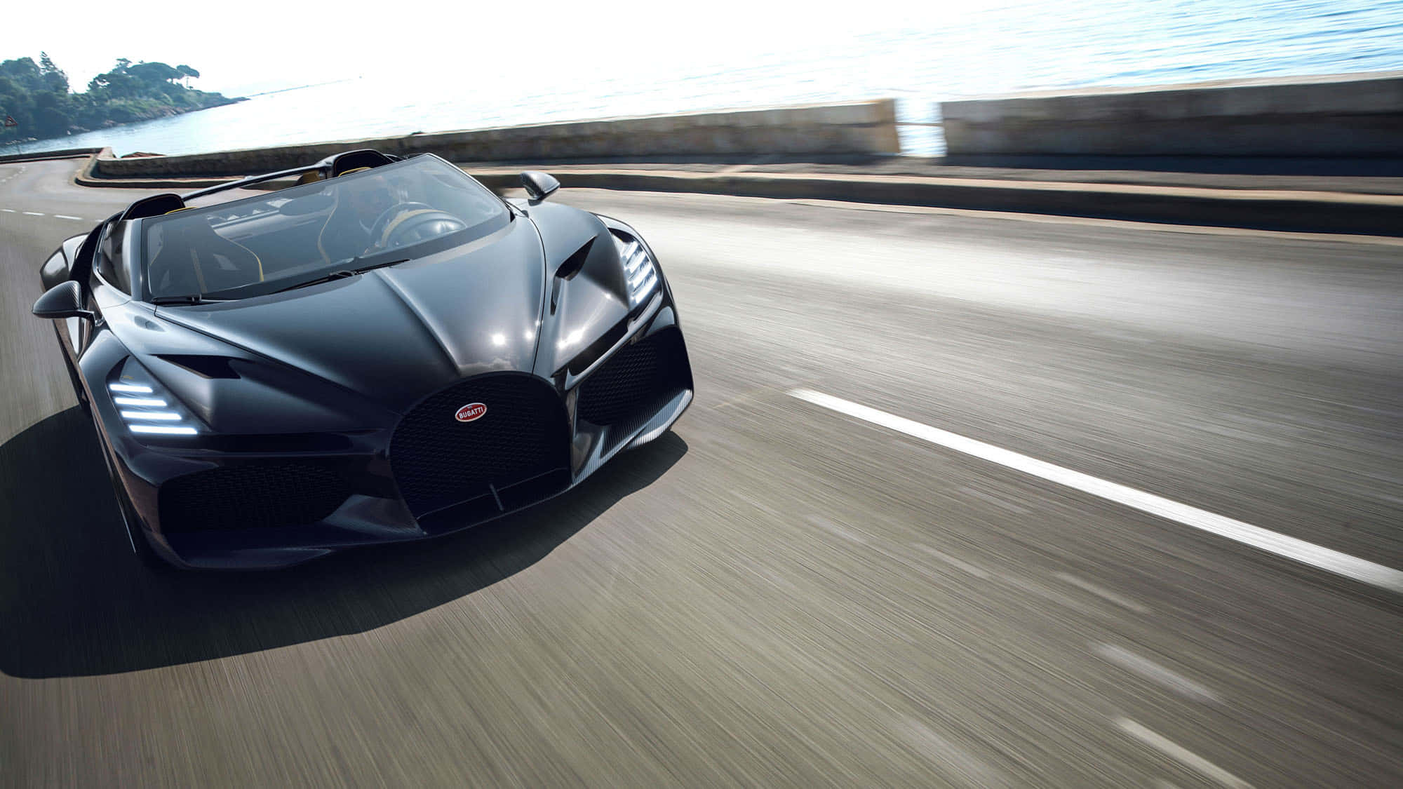 桌布 壁紙 — 一輛流線型黑色Bugatti Chiron Super Sport 300+沿著海岸公路疾馳，帶有模糊動感和海洋景觀。