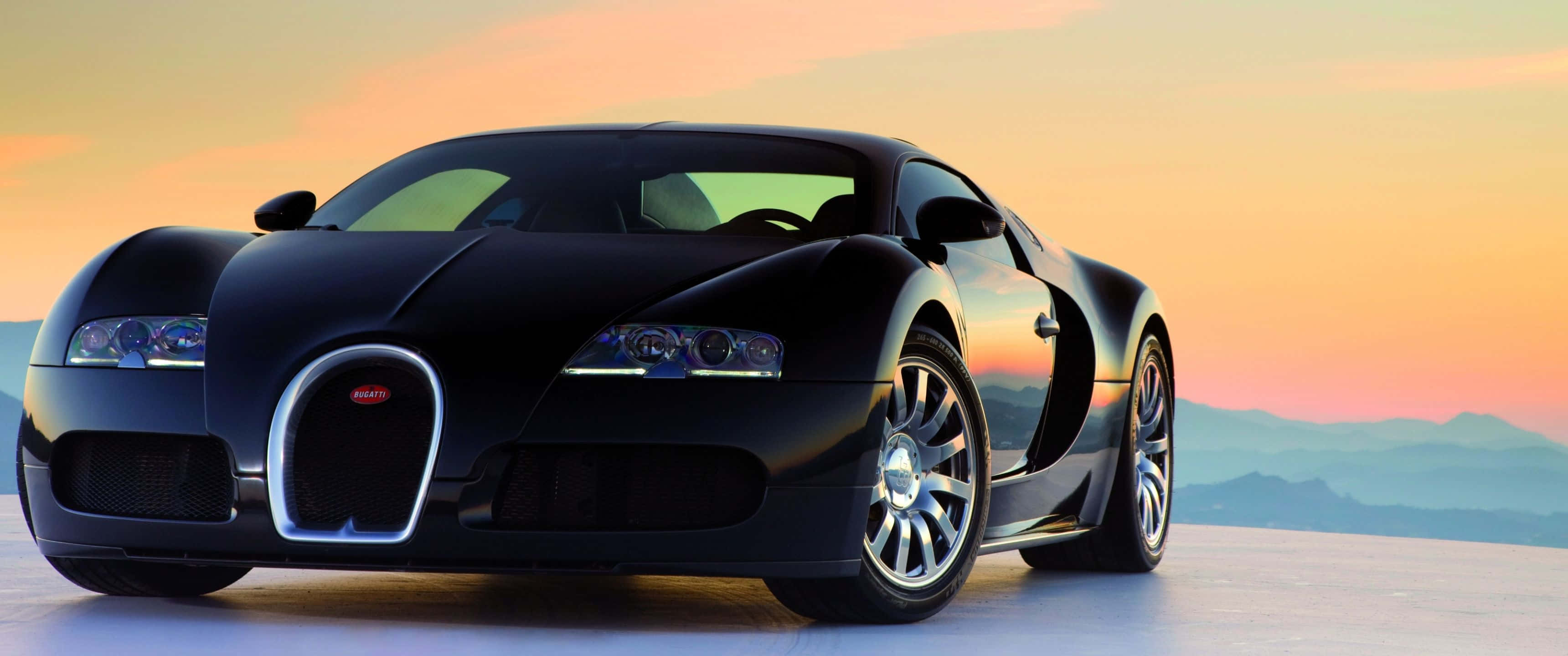 3440x1440p Bugatti 桌布 壁紙 — 一輛流線型黑色Bugatti超級跑車在 vibrant 的日落天空下閃耀，背景是遠山。