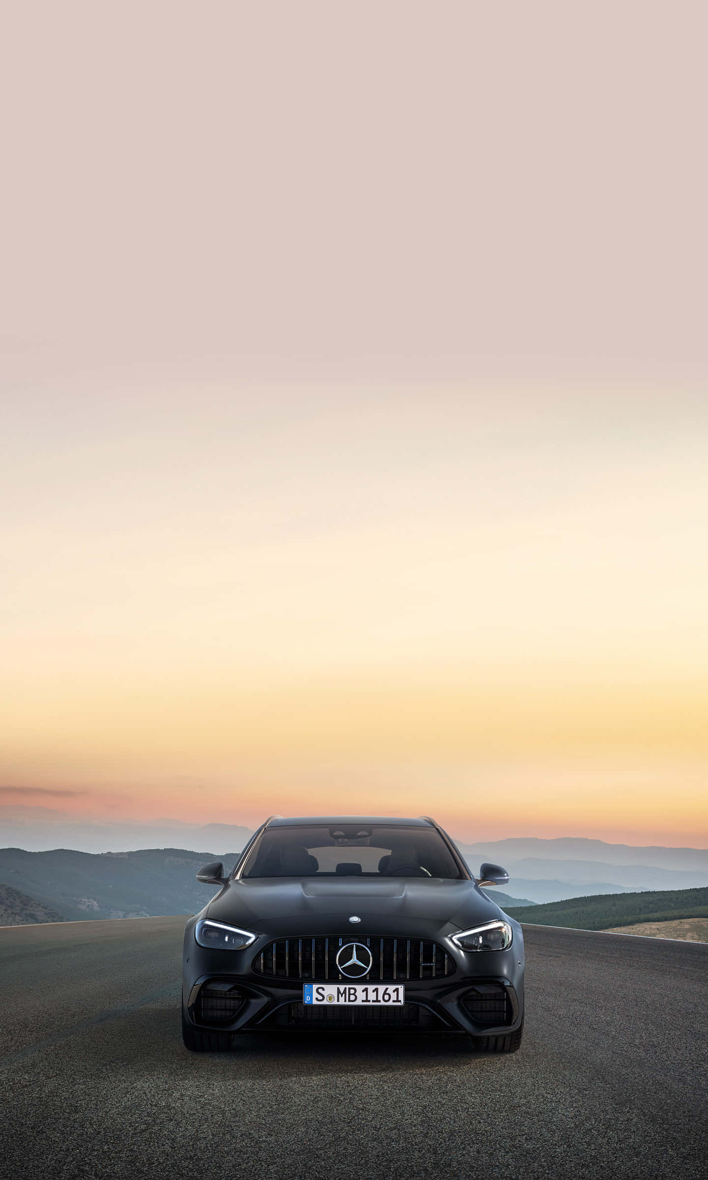 桌布 壁紙 — 一輛流線型黑色Mercedes-AMG跑車在蜿蜒的山路上，面向夕陽下柔和橙粉色的天空。