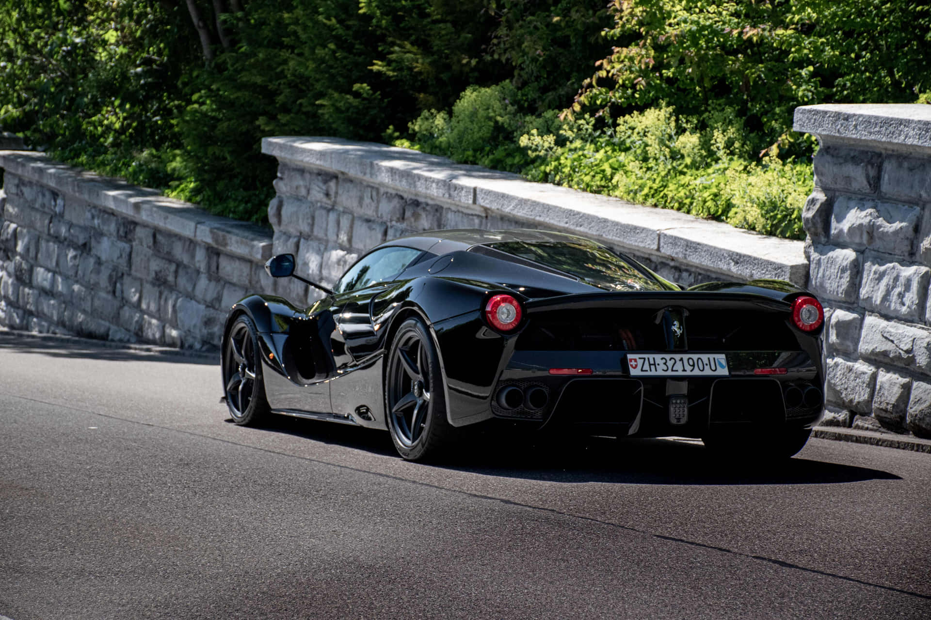 黑色法拉利 LaFerrari 在蜿蜒的山路上，有石牆和綠樹。 — 法拉利 GIF 壁紙