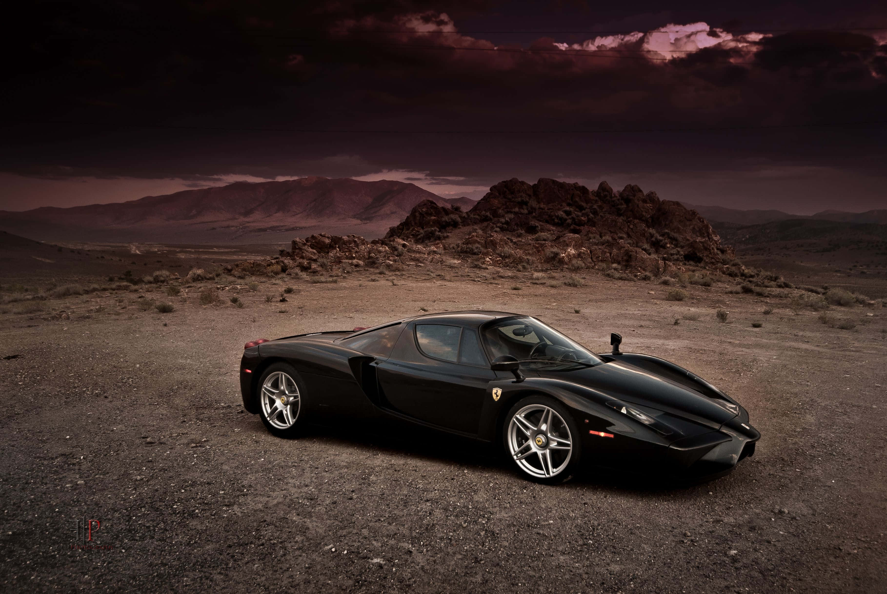 Ferrari Enzo 桌布 壁紙 — 一輛流線型黑色法拉利Enzo停泊在荒蕪的沙漠景觀中，天空佈滿戲劇性的紫色和深色雲層。