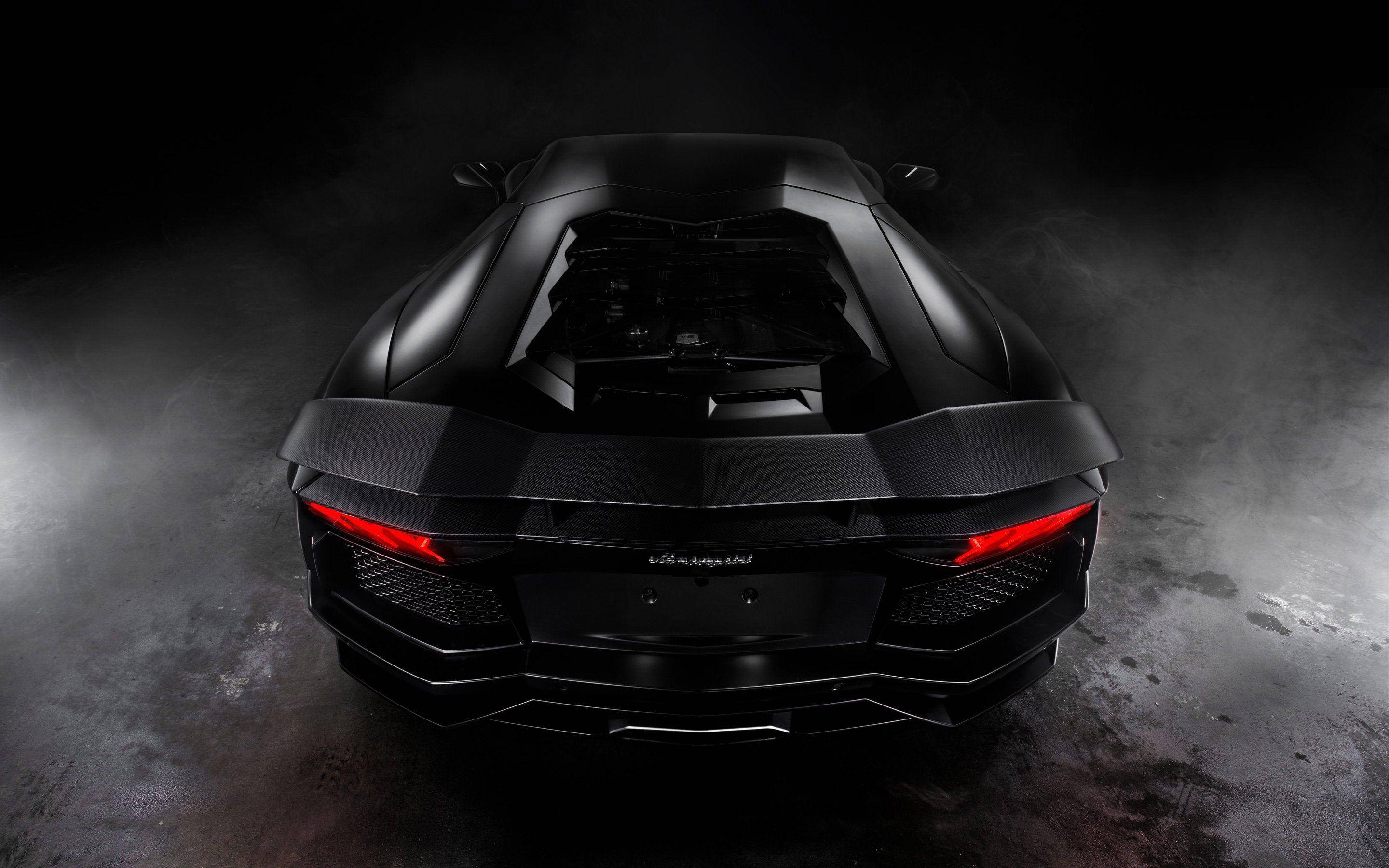 Lamborghini 4K 桌布 壁紙 — 一輛流線型黑色藍寶堅尼Aventador的後視圖，紅色尾燈在煙霧瀰漫的黑暗工作室背景下發光。
