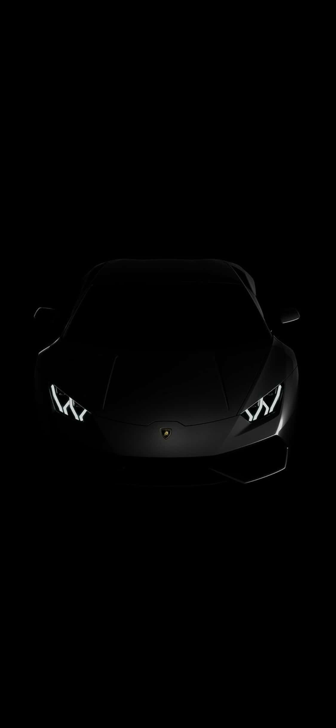 iPhone X Lamborghini 桌布 壁紙 — 一輛流線型黑色藍寶堅尼跑車，在漆黑一片中閃耀著銳利的白色車頭燈。