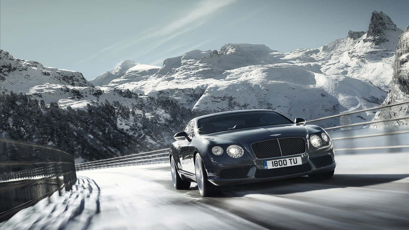 1366x768 Bentley 桌布 壁紙 — 一輛流線型黑色賓利在白雪覆蓋的山路上疾馳，背景是白雪皚皚的山峰和清澈的藍天。