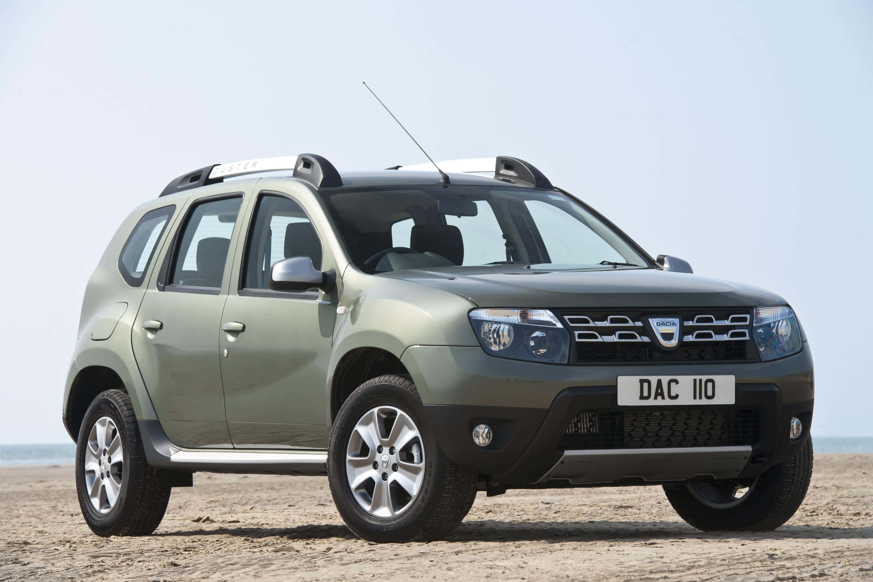 Dacia 桌布 壁紙 — 一輛消光橄欖綠色的Dacia Duster SUV停放在沙灘上，天空清澈淡藍。
