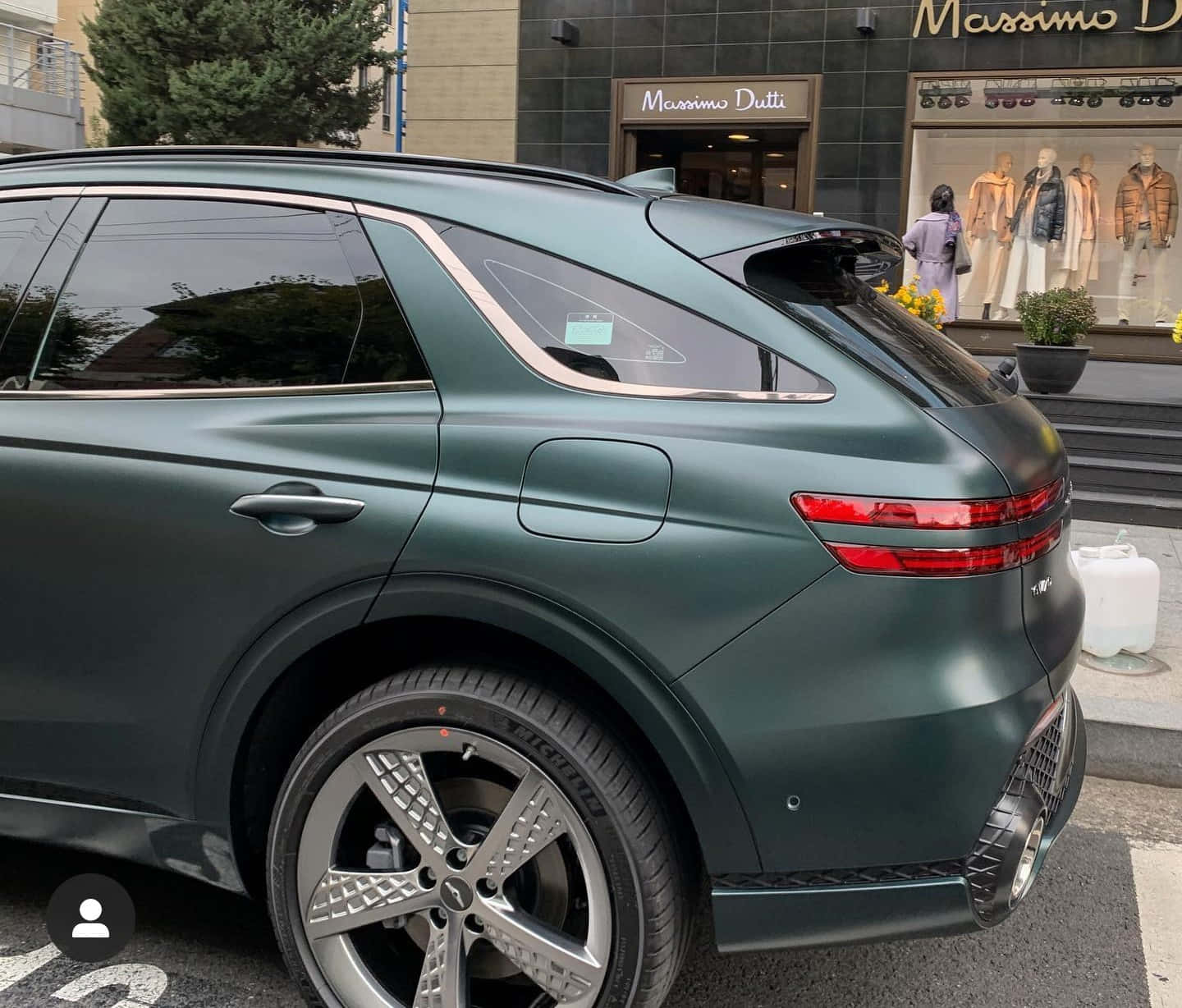 Genesis Gv70 桌布 壁紙 — 一輛消光深綠色SUV停放在城市街道上，旁邊是Massimo Dutti商店，櫥窗裡有模特兒假人。
