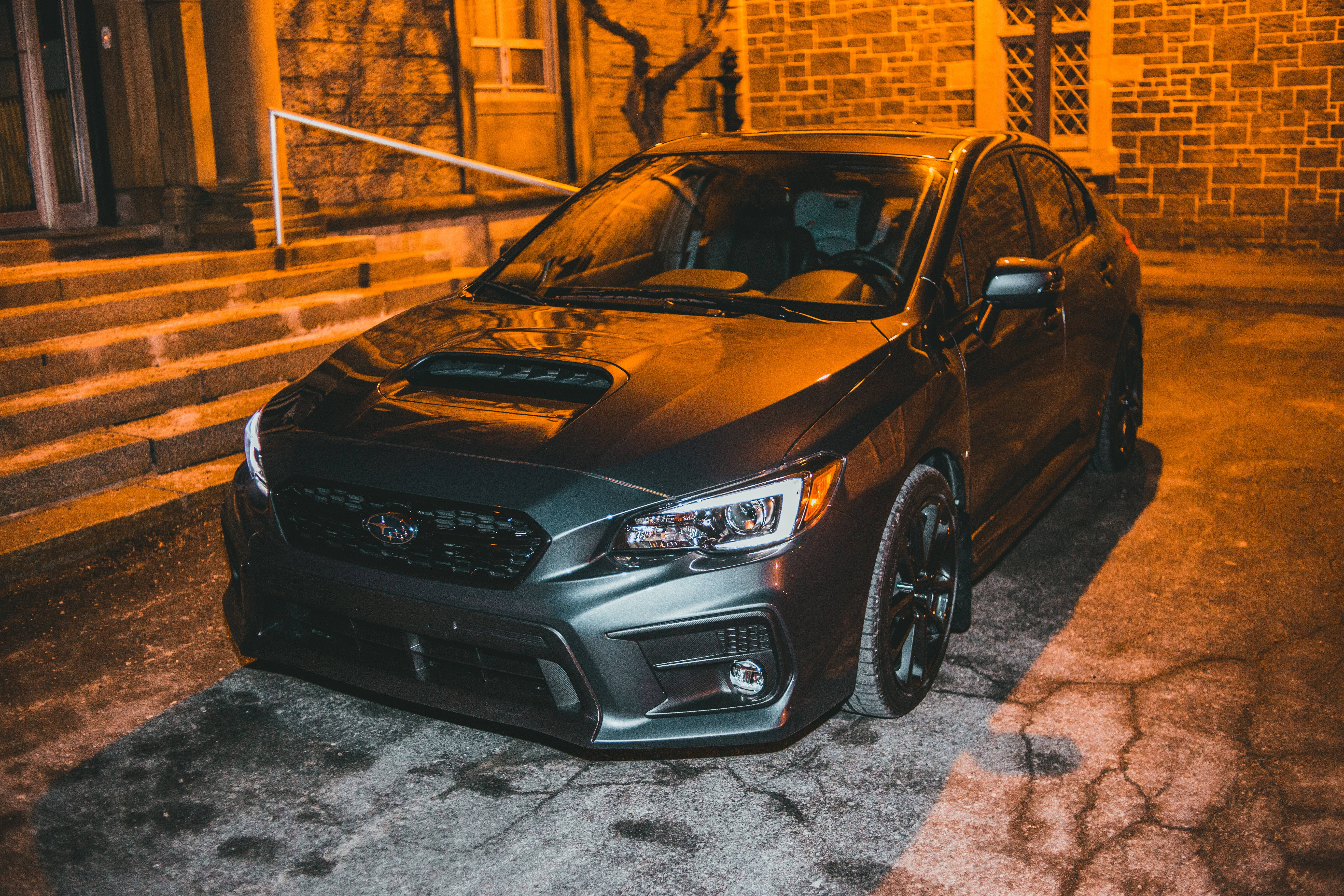 跑車 桌布 壁紙 — 一輛消光灰Subaru WRX夜晚停在裂開的路面上，被溫暖的橙色路燈照射，旁邊是石階。