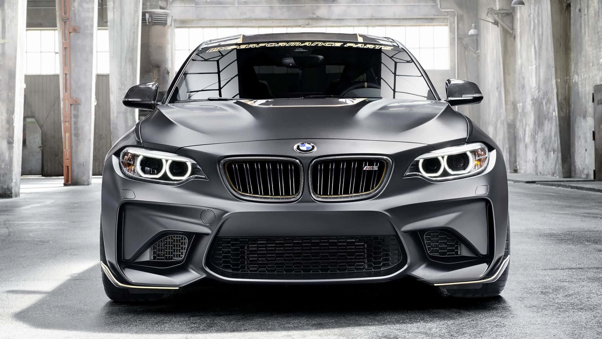 BMW 動圖 桌布 壁紙 — 一輛消光灰色BMW M2跑車搭配金色點綴，停放在混凝土工業倉庫內。