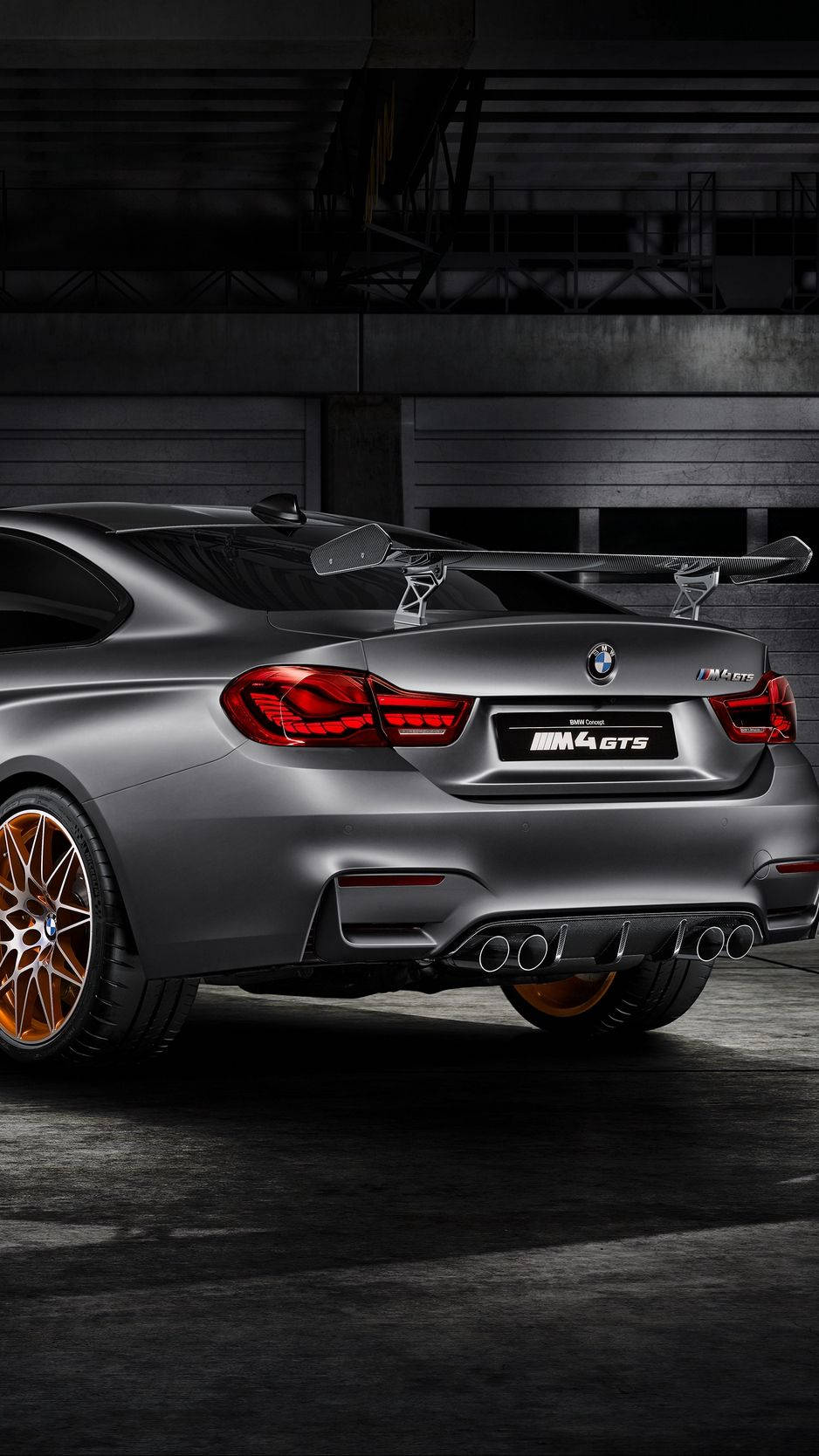 X 桌布 壁紙 — 一輛消光灰色BMW M4 GTS跑車，配備銅色輪圈和紅色尾燈，停放在昏暗的工業車庫中。