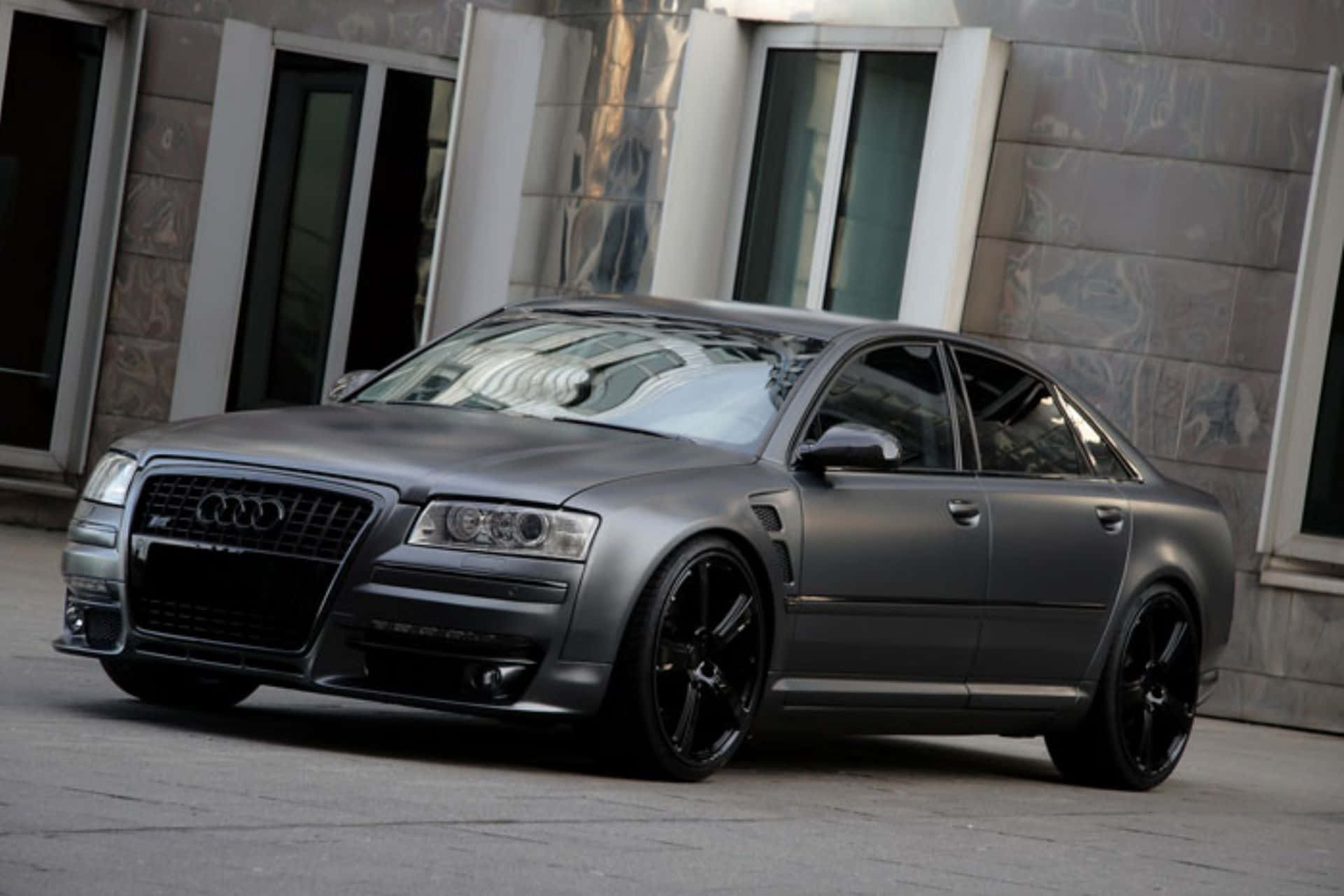 Audi S8 桌布 壁紙 — 一輛消光灰色奧迪轎車搭配黑色輪圈，停在一棟帶有反光玻璃的現代建築前。
