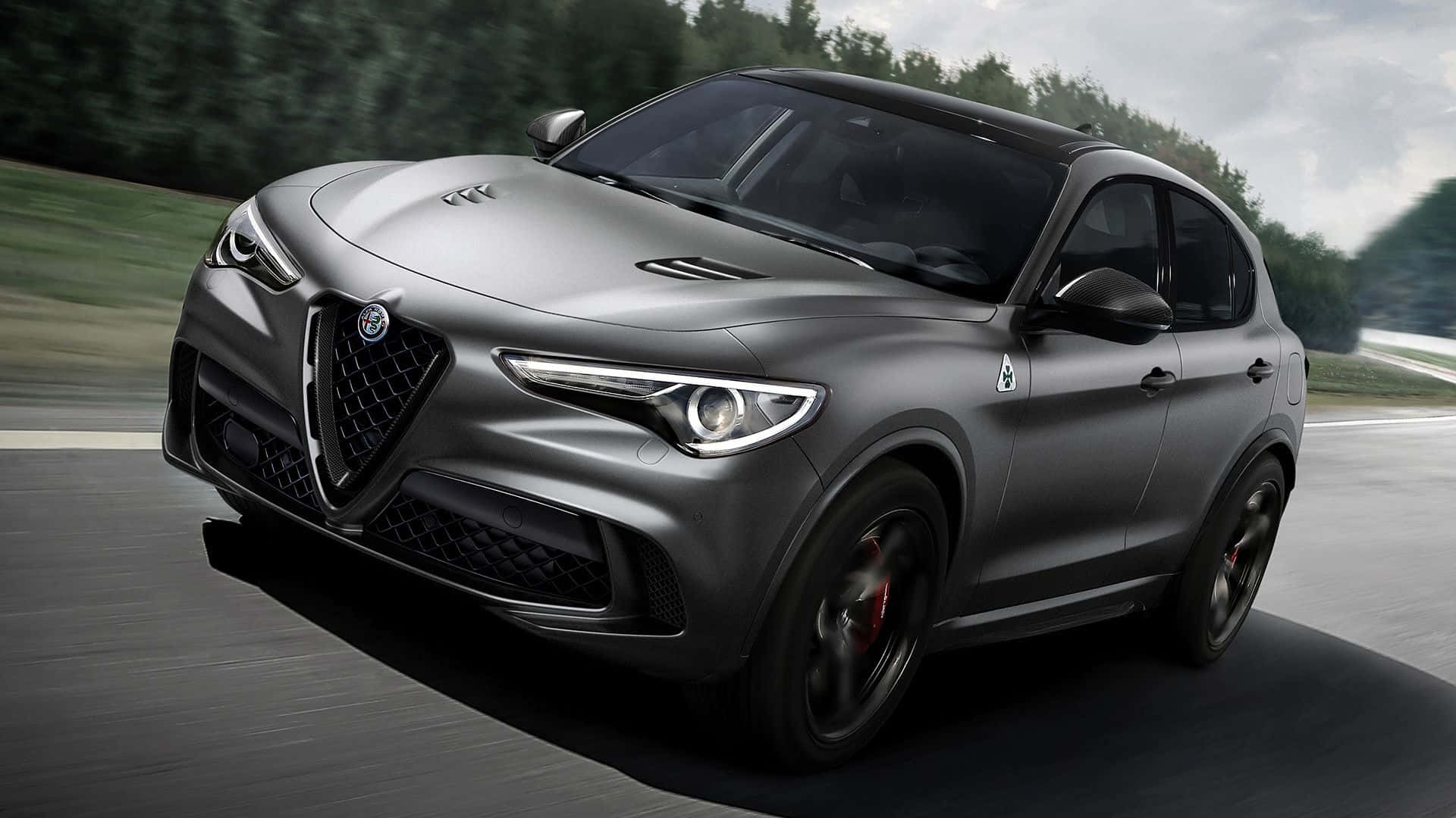 Alfa Romeo Stelvio 桌布 壁紙 — 一輛消光灰色的Alfa Romeo Stelvio Quadrifoglio在蜿蜒的道路上疾馳，背景是模糊的綠色樹木。