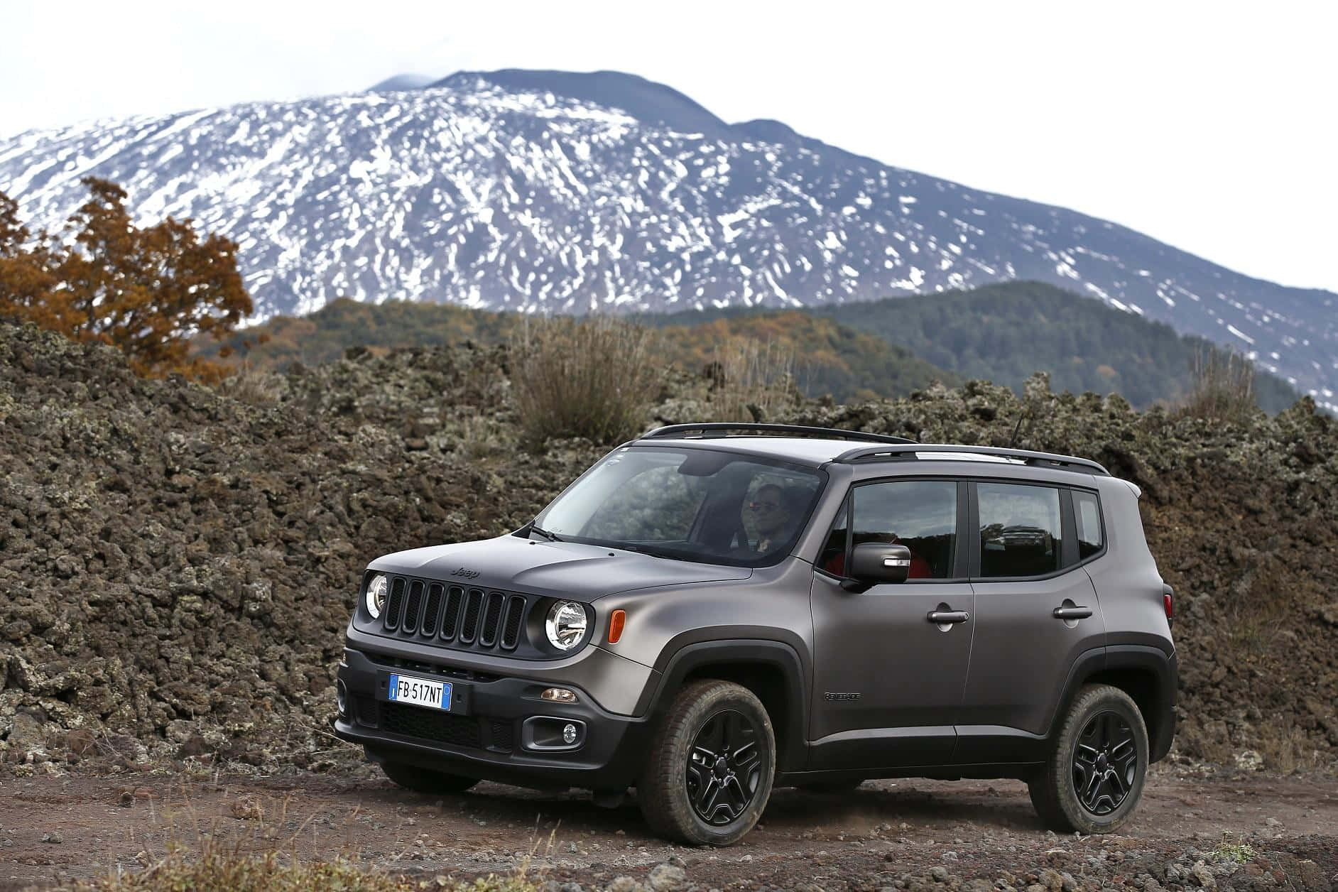 Jeep Renegade 桌布 壁紙 — 一輛消光灰色的Jeep Renegade停在崎嶇地形上，背景是覆蓋著白雪的山脈。