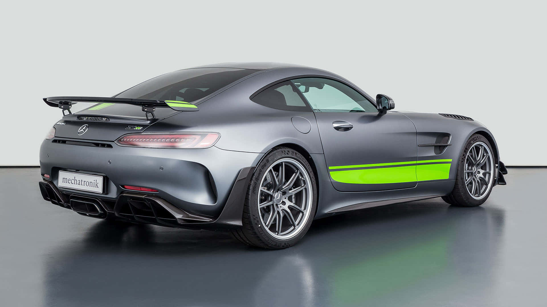 汽車 桌布 壁紙 — 一輛消光灰色的Mercedes-AMG GT R，帶有螢光綠色條紋和大型尾翼，在簡約的攝影棚環境中拍攝。