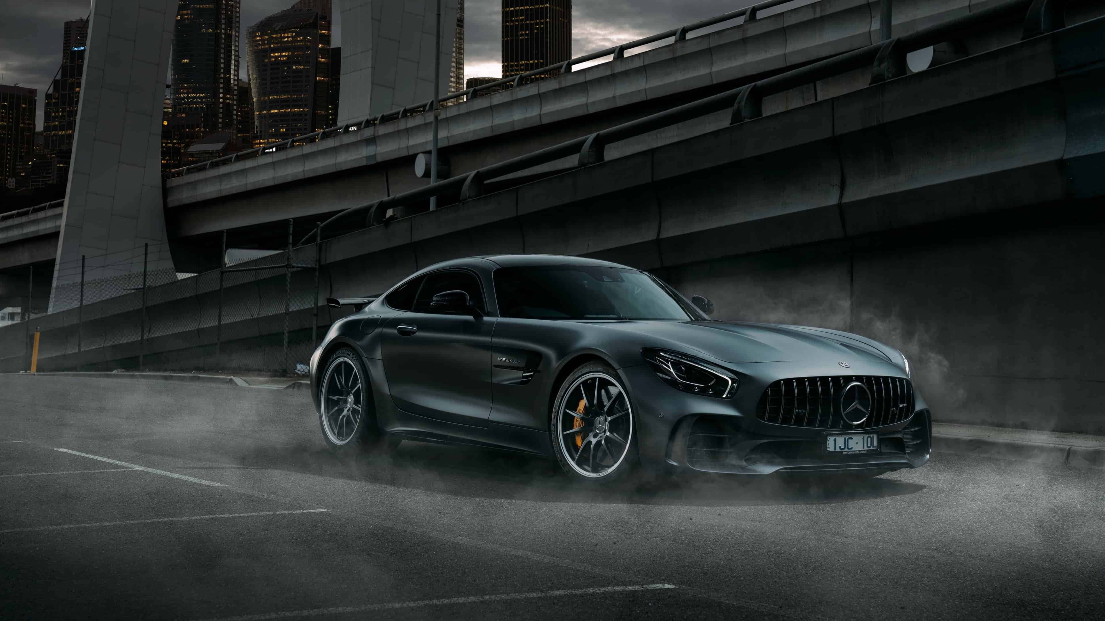 4K 奔馳壁紙 桌布 壁紙 — 一輛消光灰色的Mercedes-AMG GT在黃昏時分，於高聳天橋下的潮濕城市街道上進行甩尾。