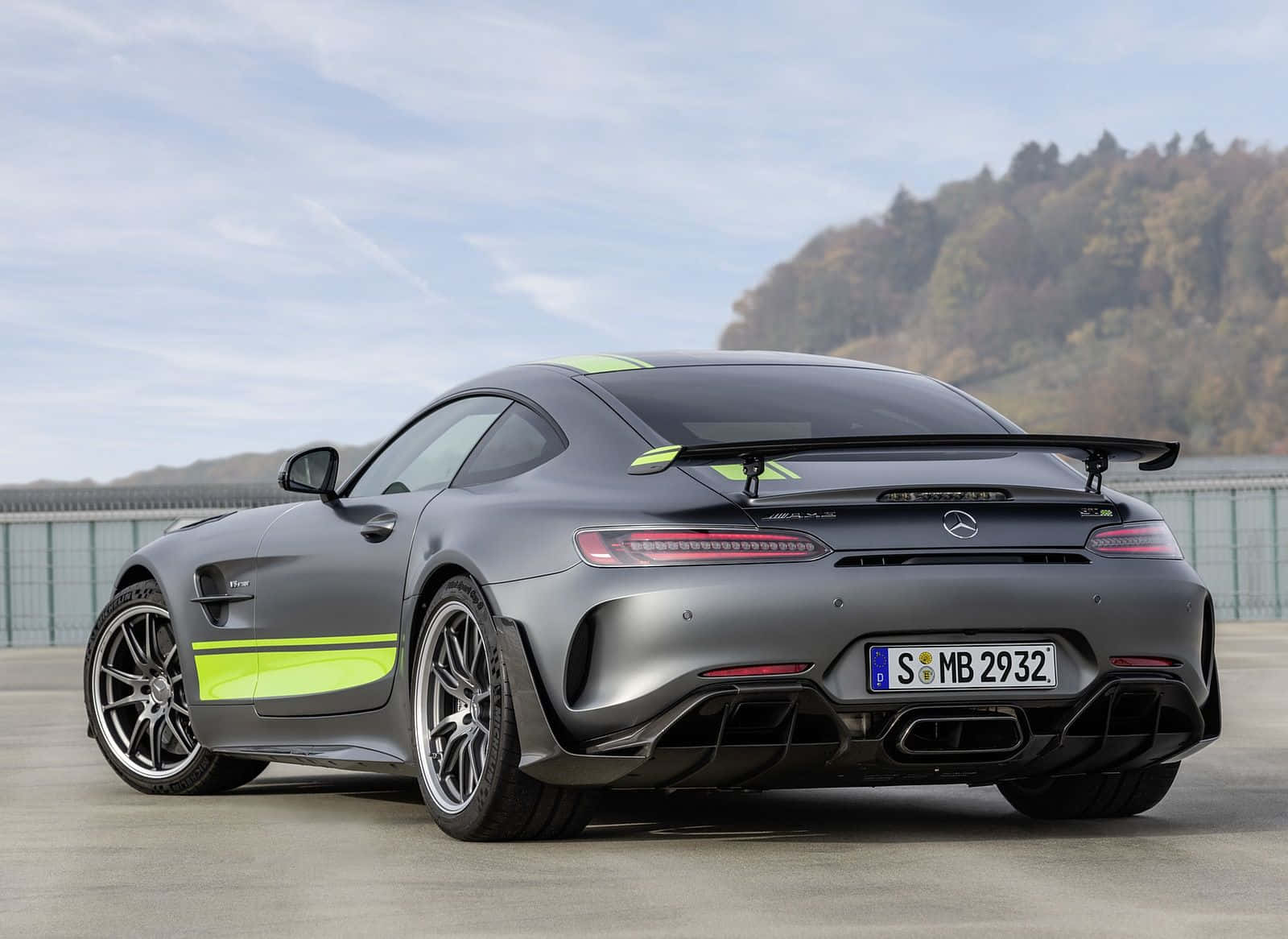 酷 桌布 壁紙 — 一輛消光灰色的梅賽德斯-AMG GT R 跑車，帶有螢光綠色點綴，停放在混凝土表面上，背景是森林覆蓋的山丘，天空部分多雲。