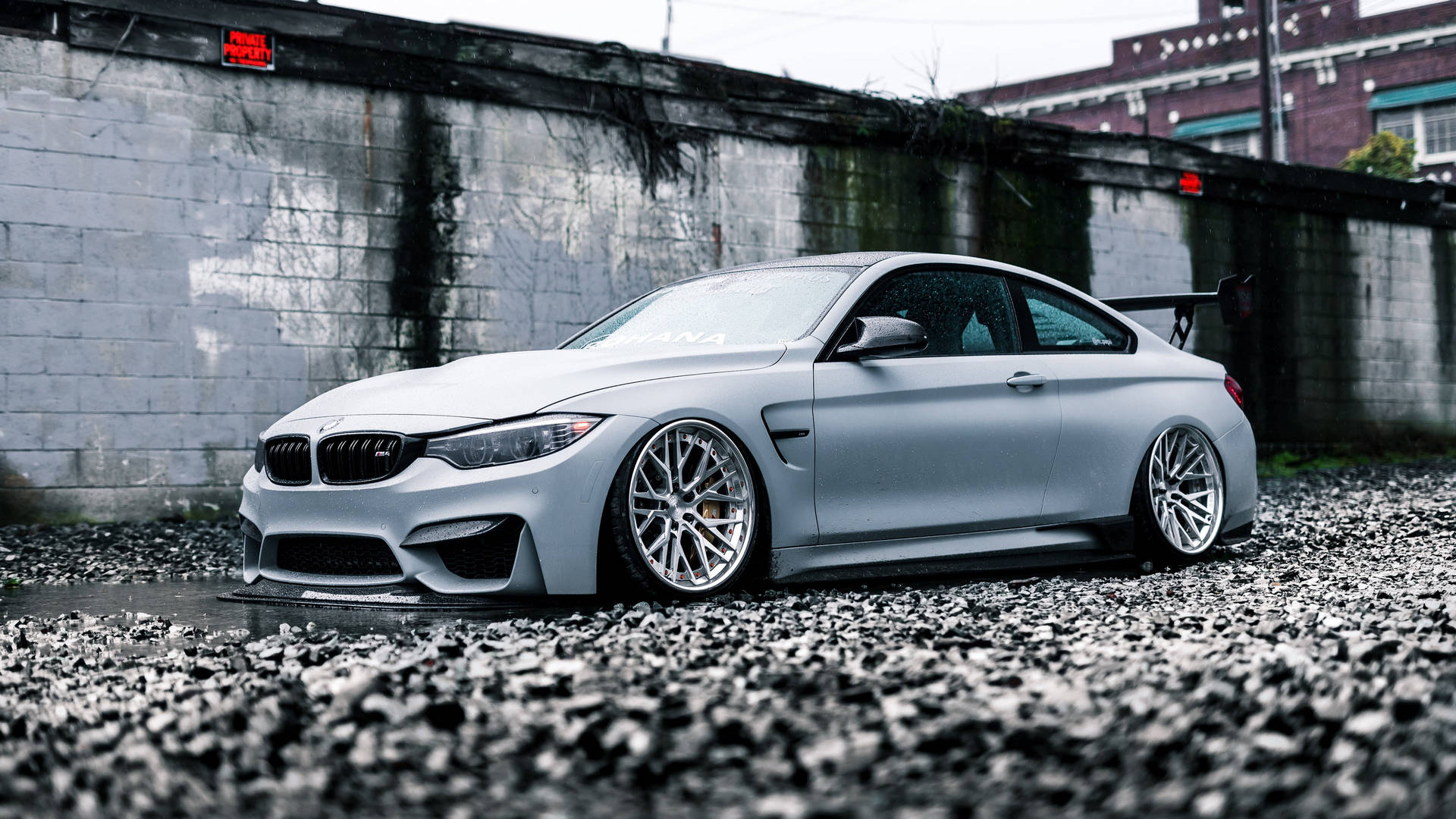 消光銀色BMW M4雙門跑車停放在碎石上，靠近混凝土牆。