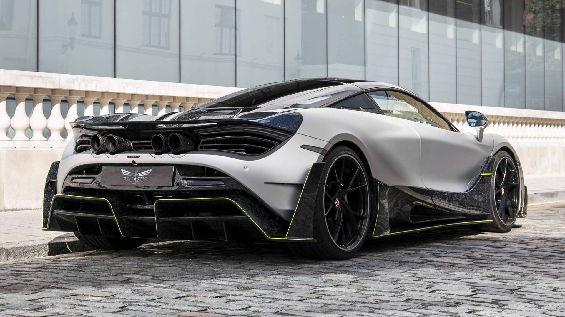 mclaren 720s 4K 桌布 壁紙 — 一輛消光銀色McLaren 720S，帶有黑色飾邊和螢光黃色點綴，停泊在現代玻璃建築旁的鵝卵石街道上。