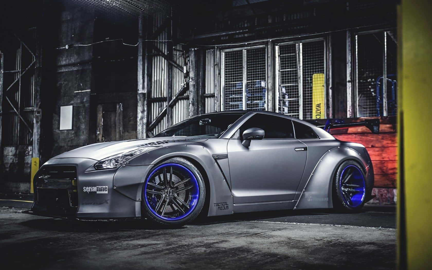 Gtr 桌布 壁紙 — 一輛消光銀色日產GT-R配備發光藍色輪圈，夜晚停泊在粗糙的工業倉庫中。