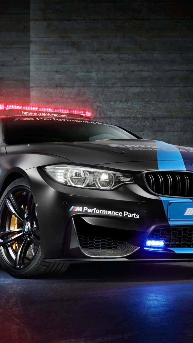 Safety Car 桌布 壁紙 — 一輛消光黑色BMW M4安全車，帶有藍色賽車條紋和紅色車頂燈，在戲劇性的攝影棚燈光下閃耀。