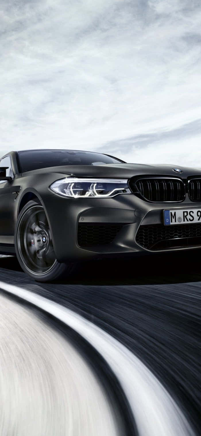 桌布 壁紙 — 一輛消光黑色BMW M5在陰天下的模糊道路上疾駛，動態模糊強調了速度。