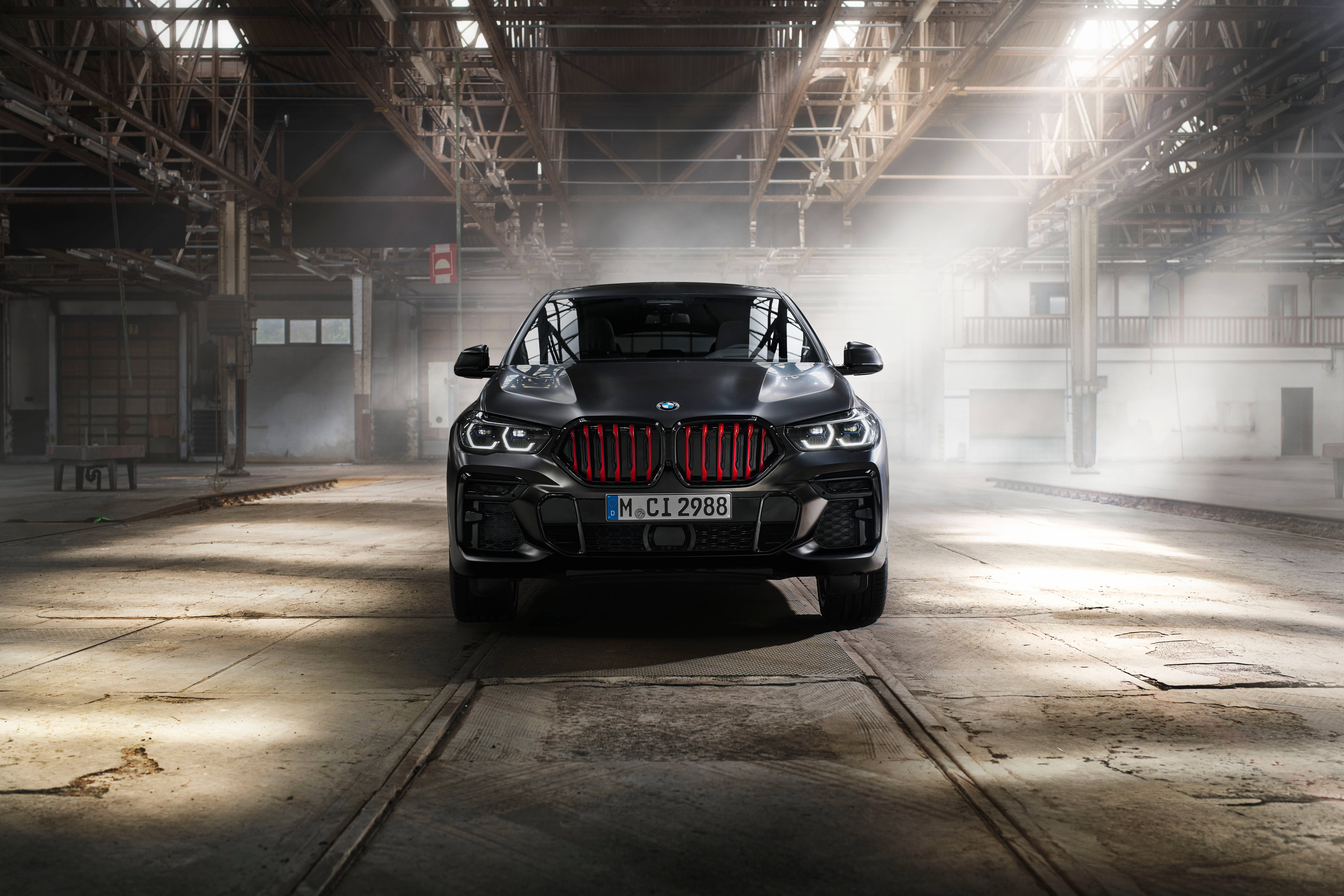 Black Bmw 桌布 壁紙 — 一輛消光黑色BMW X6 M Competition搭配發光紅色水箱護罩，戲劇性地矗立在灰塵滿佈的工業倉庫中，光線從上方照射。