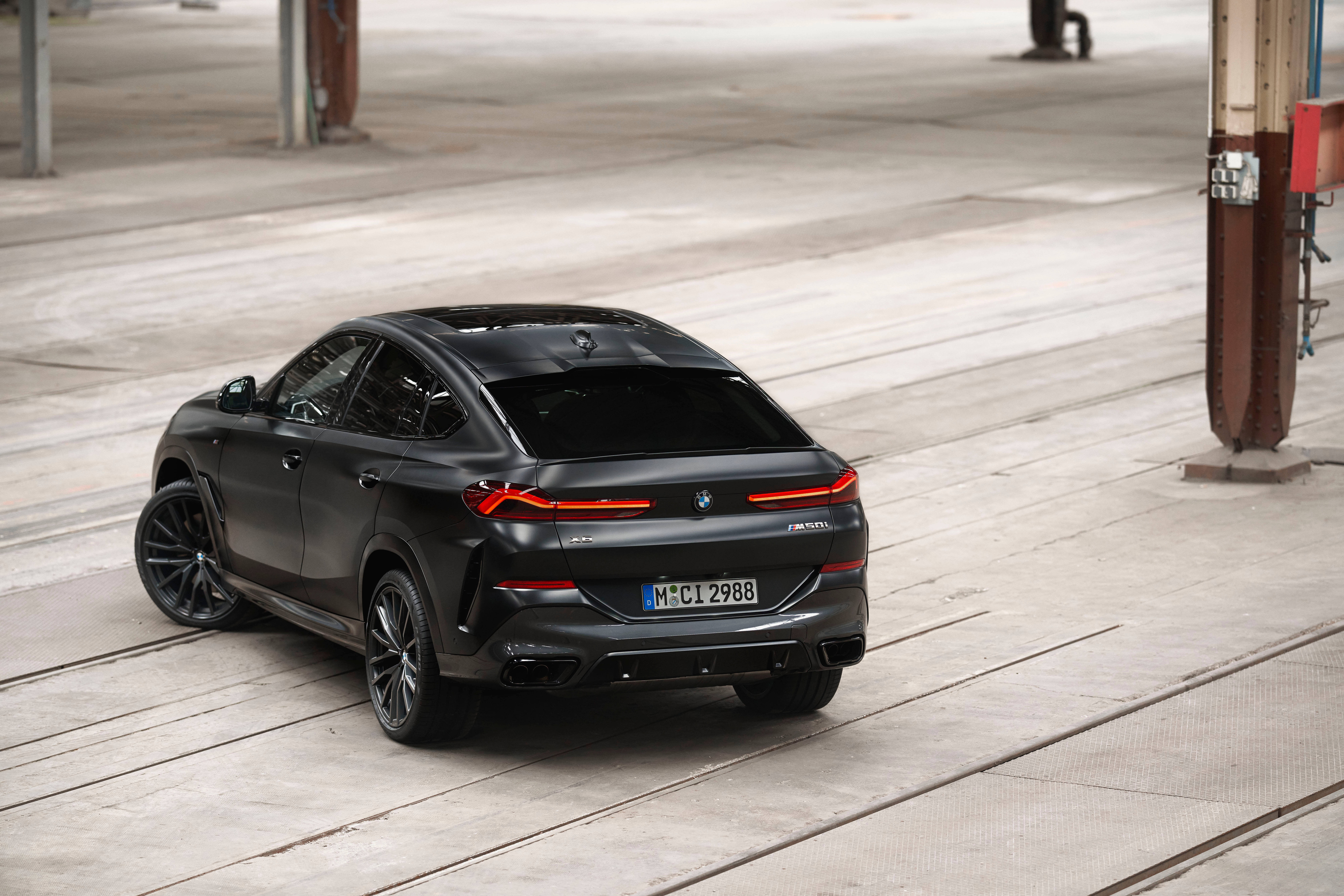 Black Bmw 桌布 壁紙 — 一輛消光黑色BMW X6 M停放在工業橫樑下的混凝土軌道上，紅色尾燈發光。