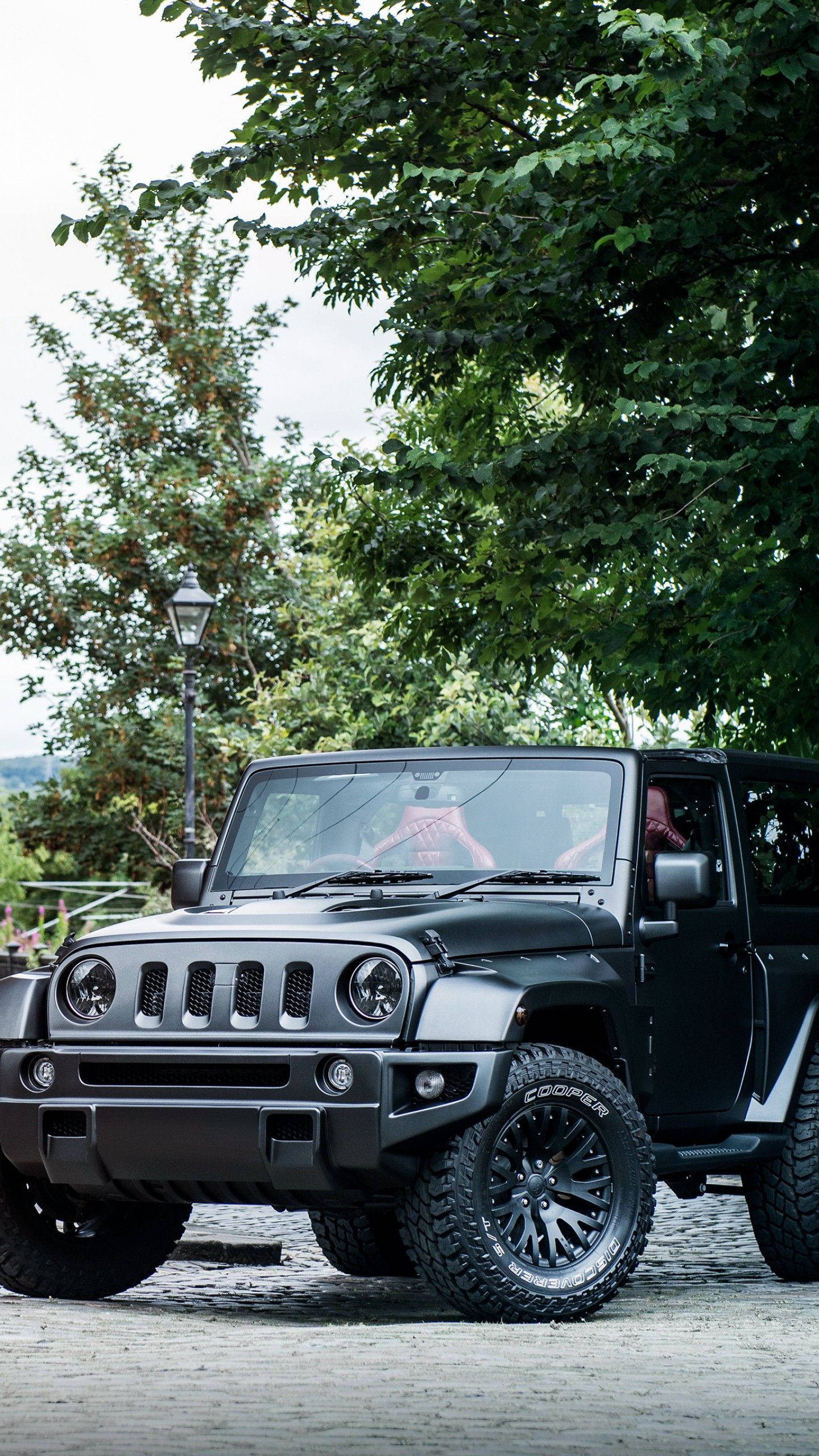 Black Jeep 桌布 壁紙 — 一輛消光黑色Jeep Wrangler停在鵝卵石路上，上方是茂密的綠樹，車內有一個人。