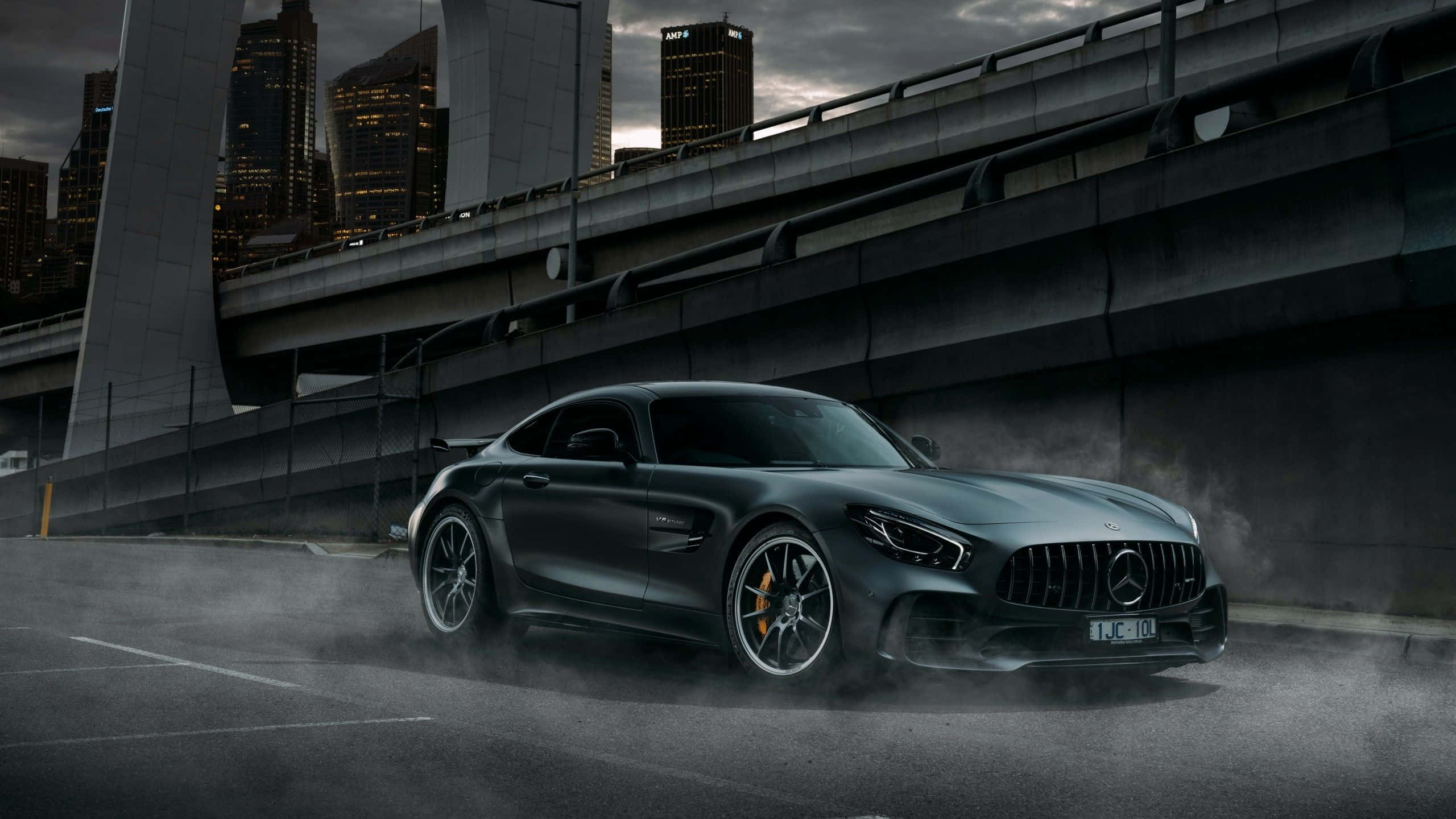 桌布 壁紙 — 一輛消光黑色的 Mercedes-AMG GT 跑車在黃昏時分，在雄偉的高架橋下的潮濕城市道路上飄移。