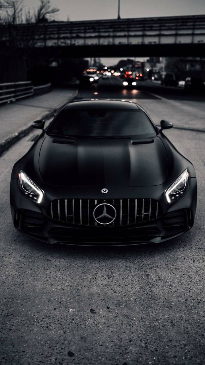 Amg 桌布 壁紙 — 一輛消光黑色的 Mercedes-AMG GT 跑車在橋下昏暗的城市道路上向前行駛，遠處模糊的交通號誌閃爍著光芒。