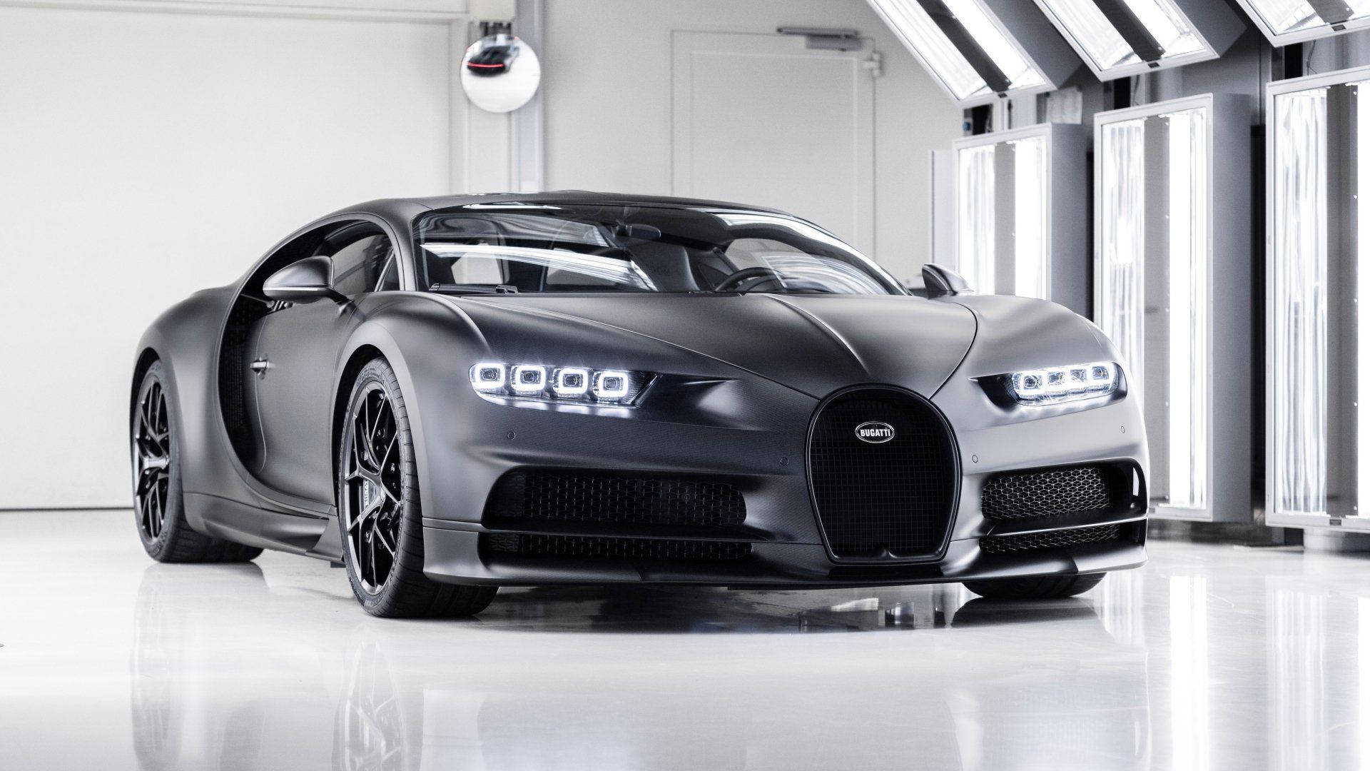 Cool Bugatti 桌布 壁紙 — 一輛消光黑色的Bugatti Chiron跑車在明亮的攝影棚燈光下，在簡約的白色車庫中閃閃發光。