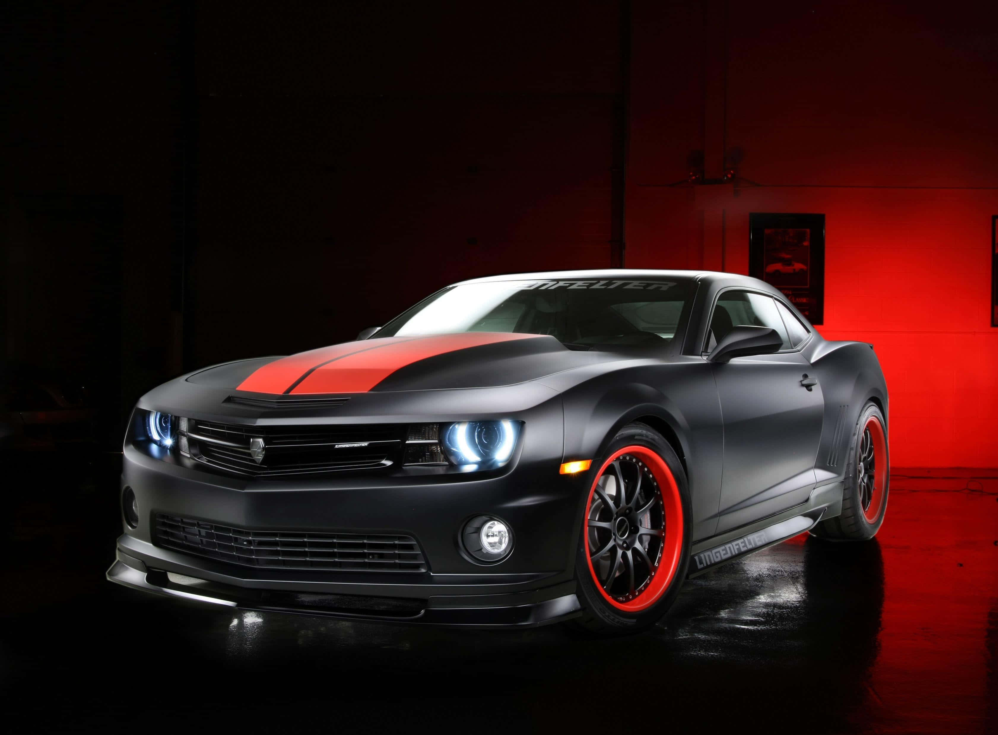 Chevrolet 桌布 壁紙 — 一輛消光黑色的Camaro，帶有醒目的紅色條紋和輪圈，在戲劇性的紅色工作室燈光下閃耀。