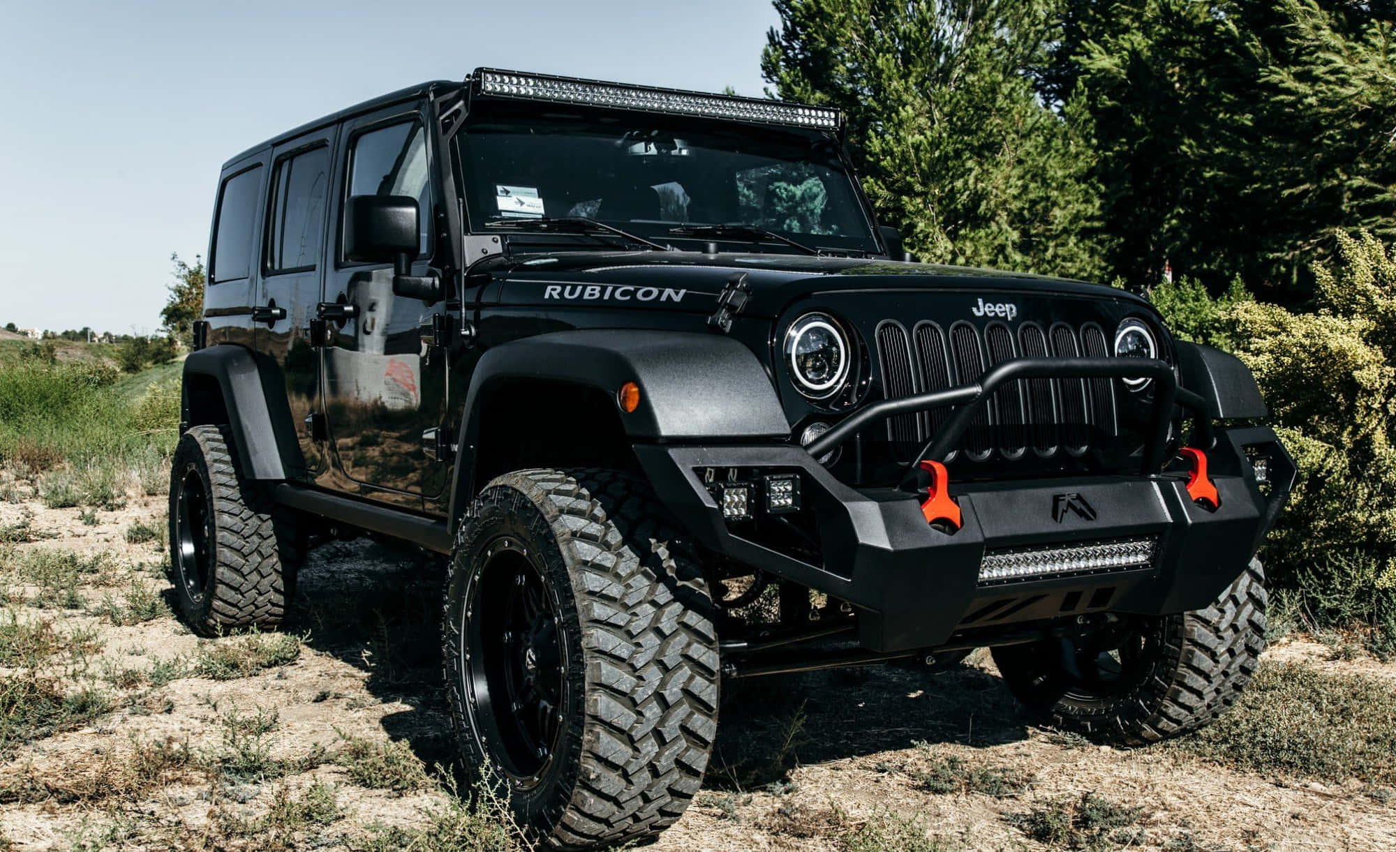 黑色吉普車 桌布 壁紙 — 一輛消光黑色的Jeep Rubicon，配備超大輪胎和橙色救援點，在明亮的日光下堅固地立在乾草上。