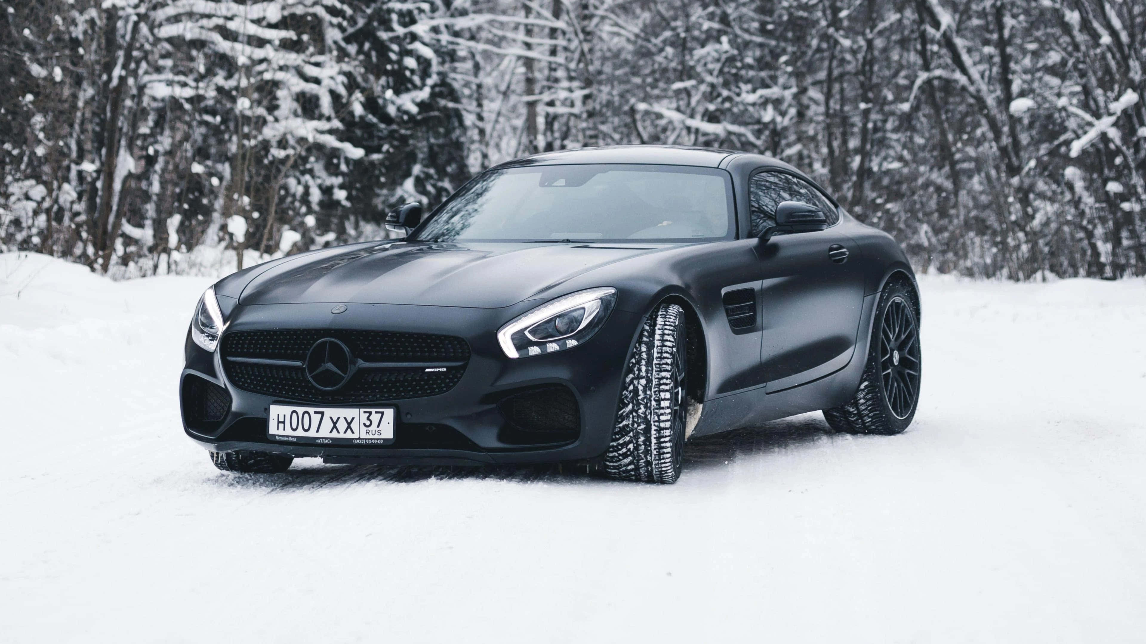 Mercedes 桌布 壁紙 — 一輛消光黑色的Mercedes-AMG GT跑車配備雪地輪胎，停在積雪的森林道路上。