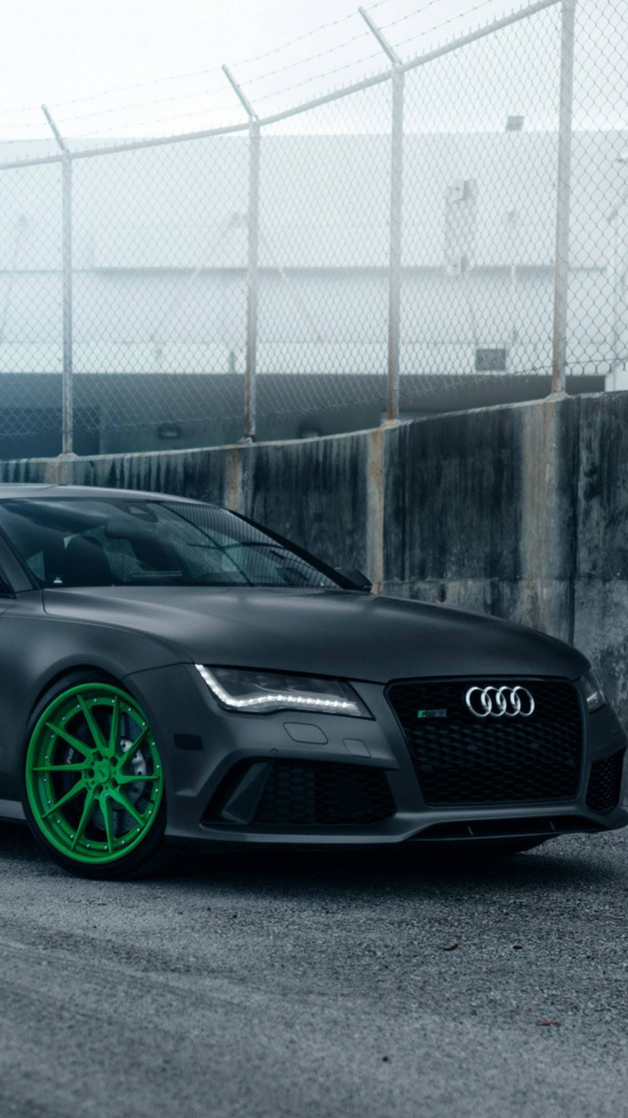 cars 桌布 壁紙 — 一輛消光黑色的奧迪跑車，帶有鮮綠色車輪，停在工業區的鐵絲網圍欄附近，環境霧氣瀰漫。