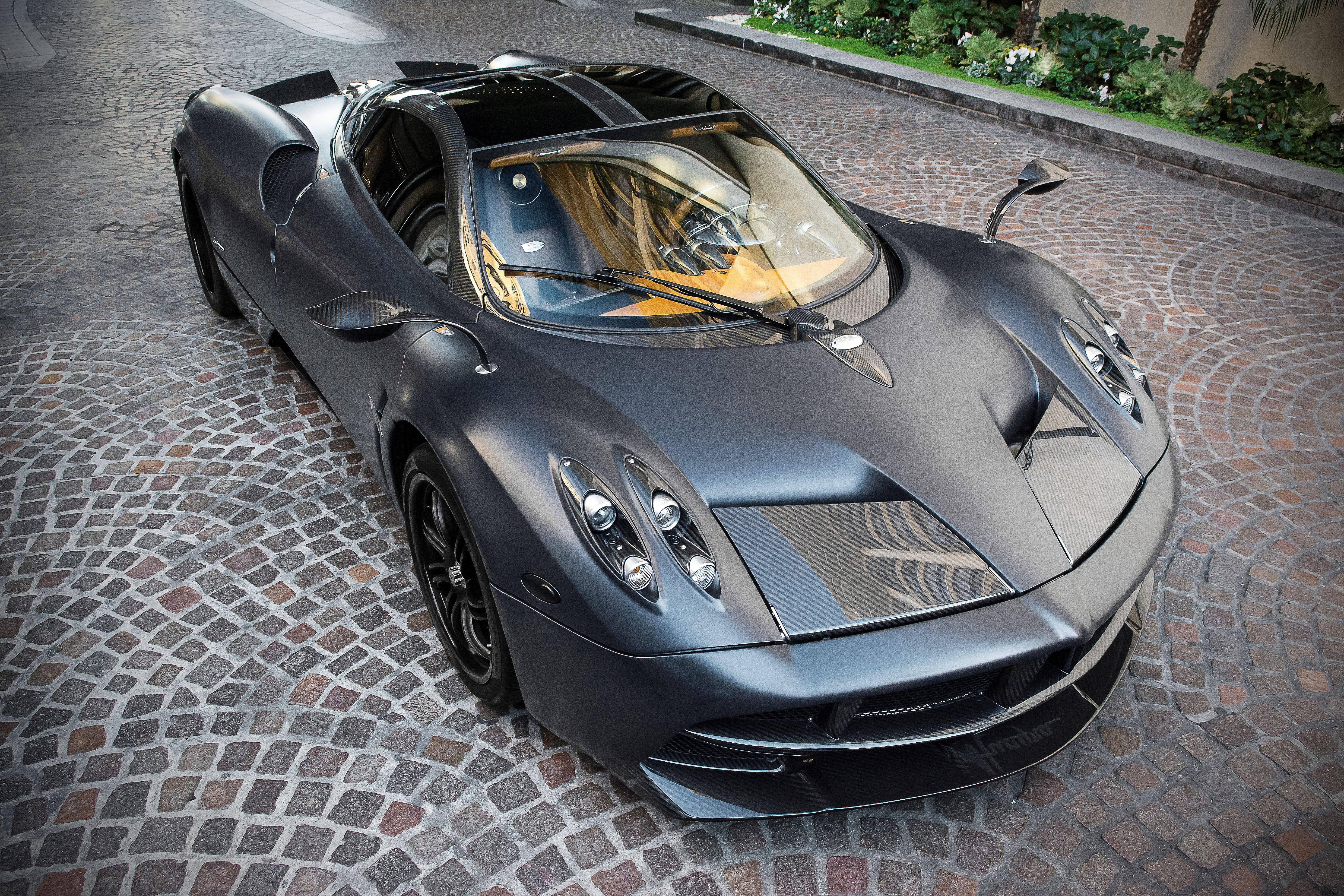 Pagani 桌布 壁紙 — 一輛消光黑色的帕加尼 Huayra 跑車停在鵝卵石車道上，背景是茂密的綠植。