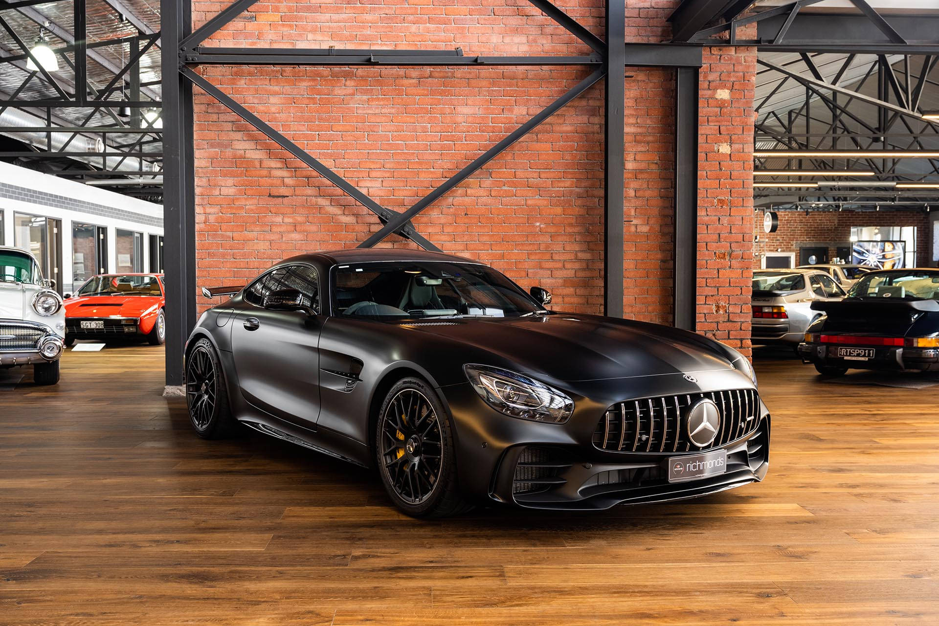 Gtr 桌布 壁紙 — 一輛消光黑色的梅賽德斯-AMG GT S轎跑車在磚木質樸的汽車展示間中，在明亮燈光下閃閃發光。
