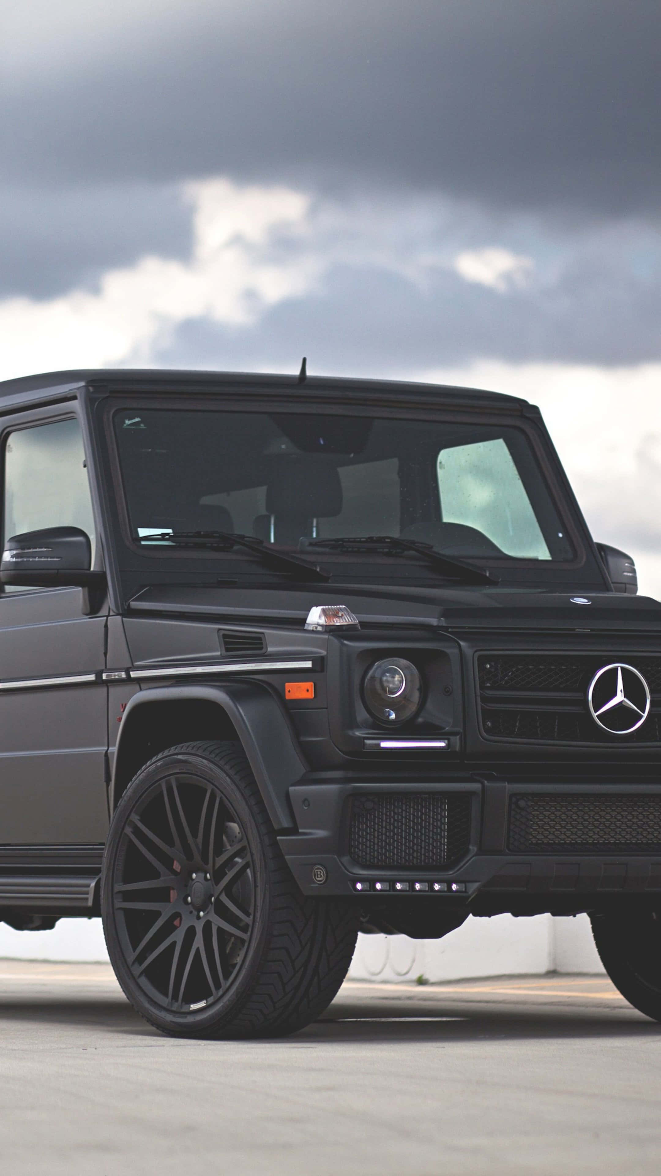 Mercedes Car 4K 桌布 壁紙 — 一輛消光黑色的梅賽德斯G-Wagen在戲劇性的多雲天空下，停在混凝土表面上。