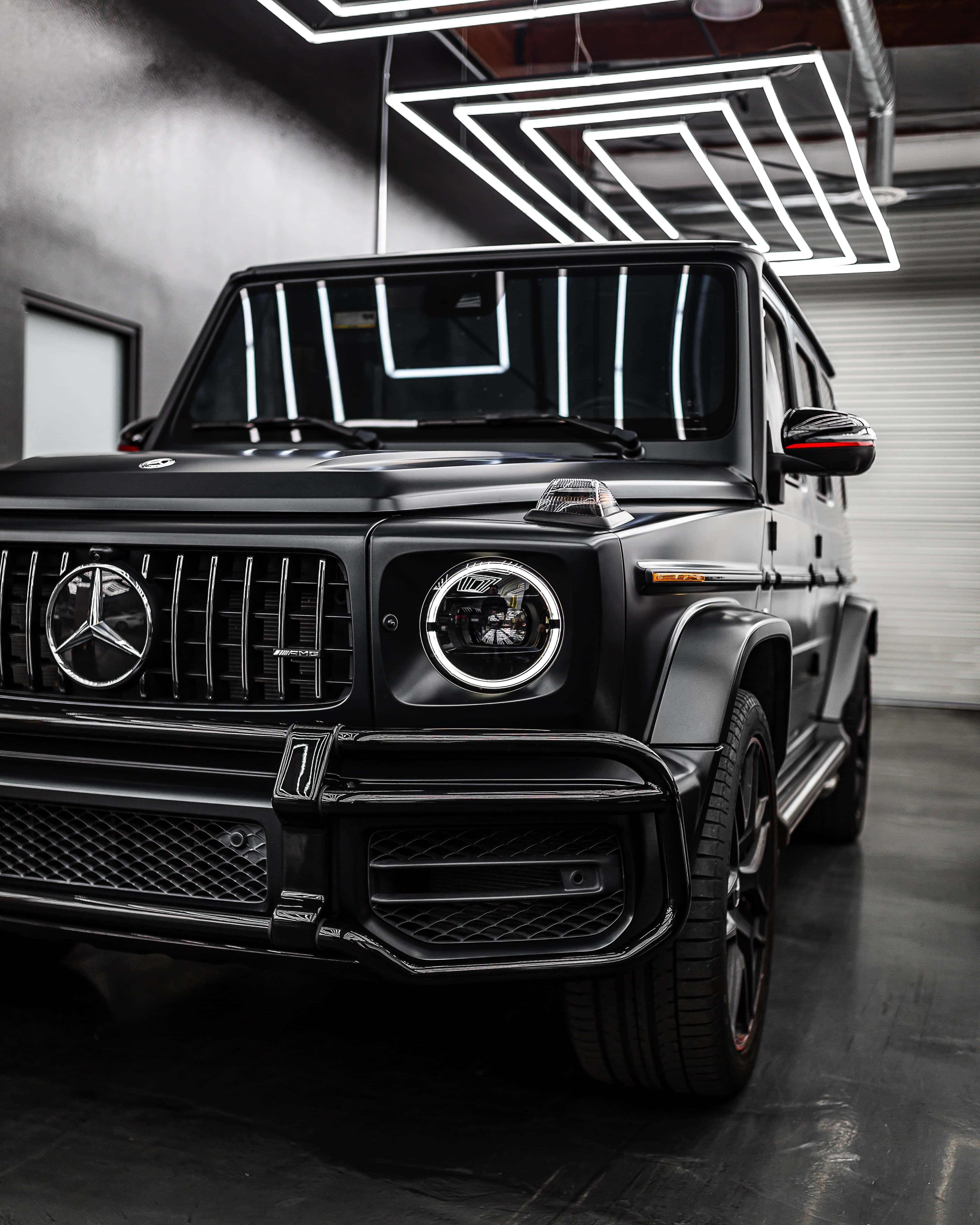 Mercedes 桌布 壁紙 — 一輛消光黑色的梅賽德斯G-Wagen SUV在時尚現代車庫的幾何霓虹燈下閃閃發光。