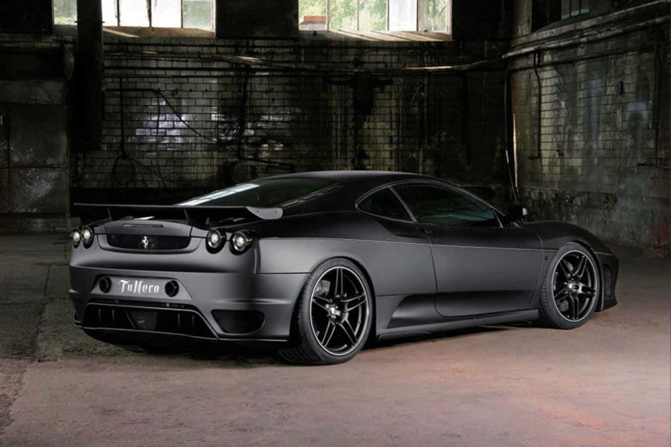 Ferrari F430 桌布 壁紙 — 一輛消光黑色的法拉利跑車配備客製化輪圈，戲劇性地停放在昏暗骯髒的工業倉庫中。
